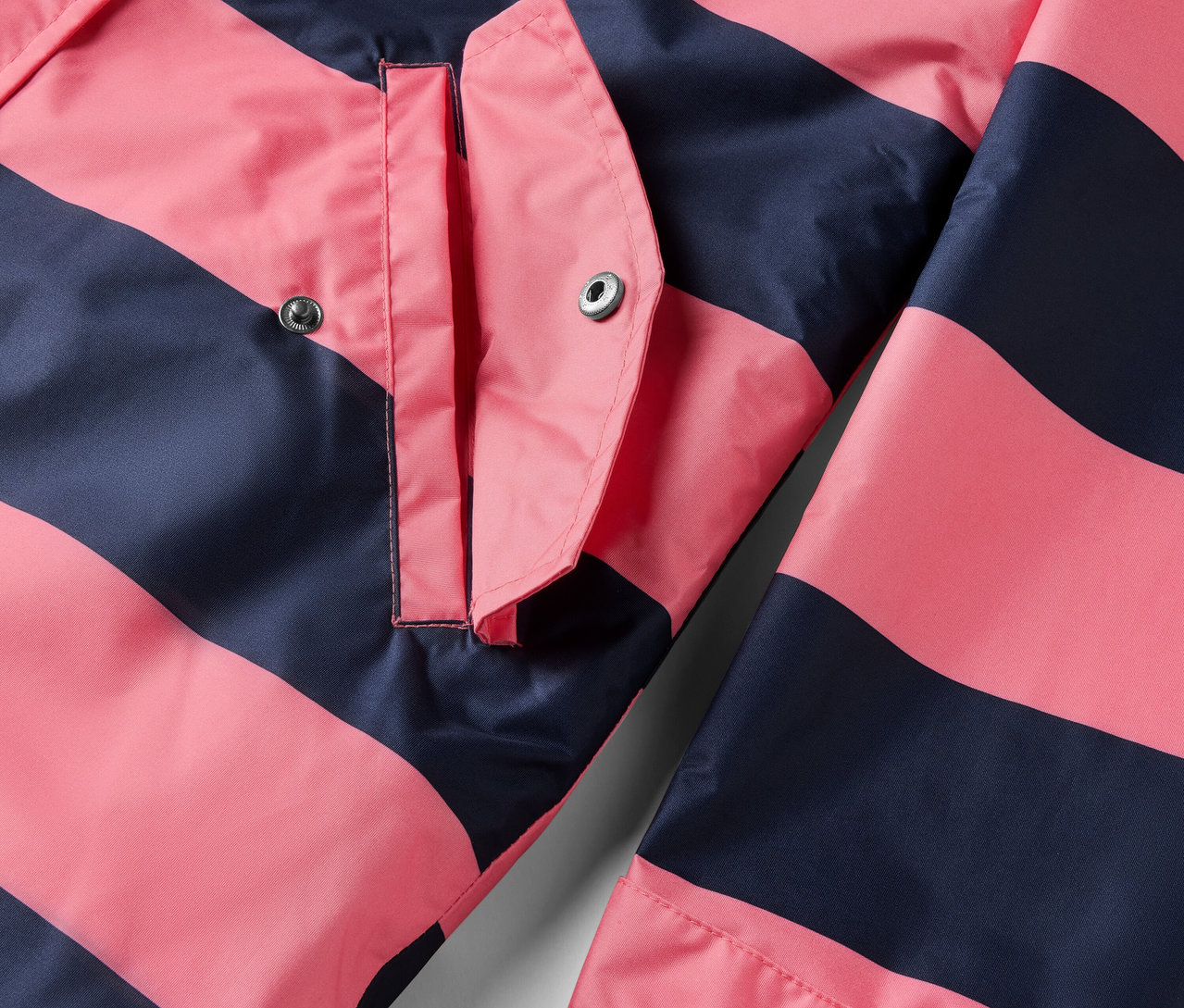 Detailansicht einer 3-in-1-Regenjacke mit rosa und dunkelblauen Streifen und einer Tasche.