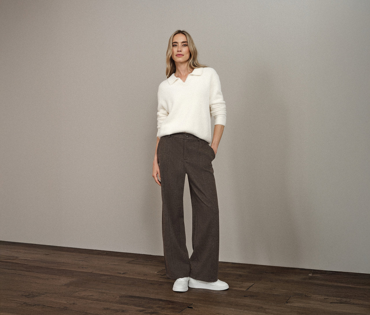 Frau steht mit den Händen in den Hosentaschen und trägt einen Street One Strickpullover mit Polokragen, eine braune Hose und weiße Schuhe.