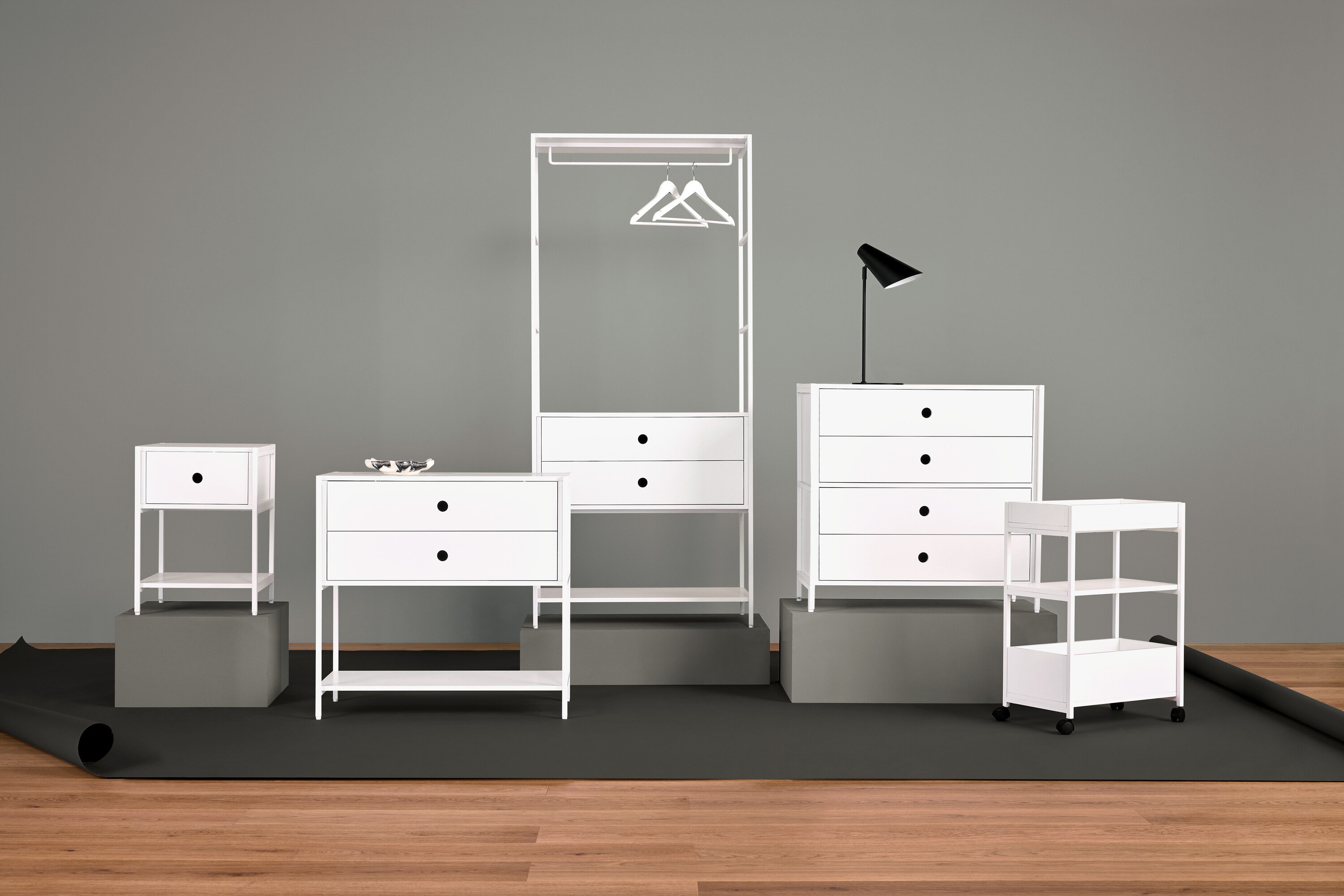 Anordnung von weißen Möbeln mit Nachttisch, Kommode mit Schubladen, Kleiderständer, Lampe und Regalen.