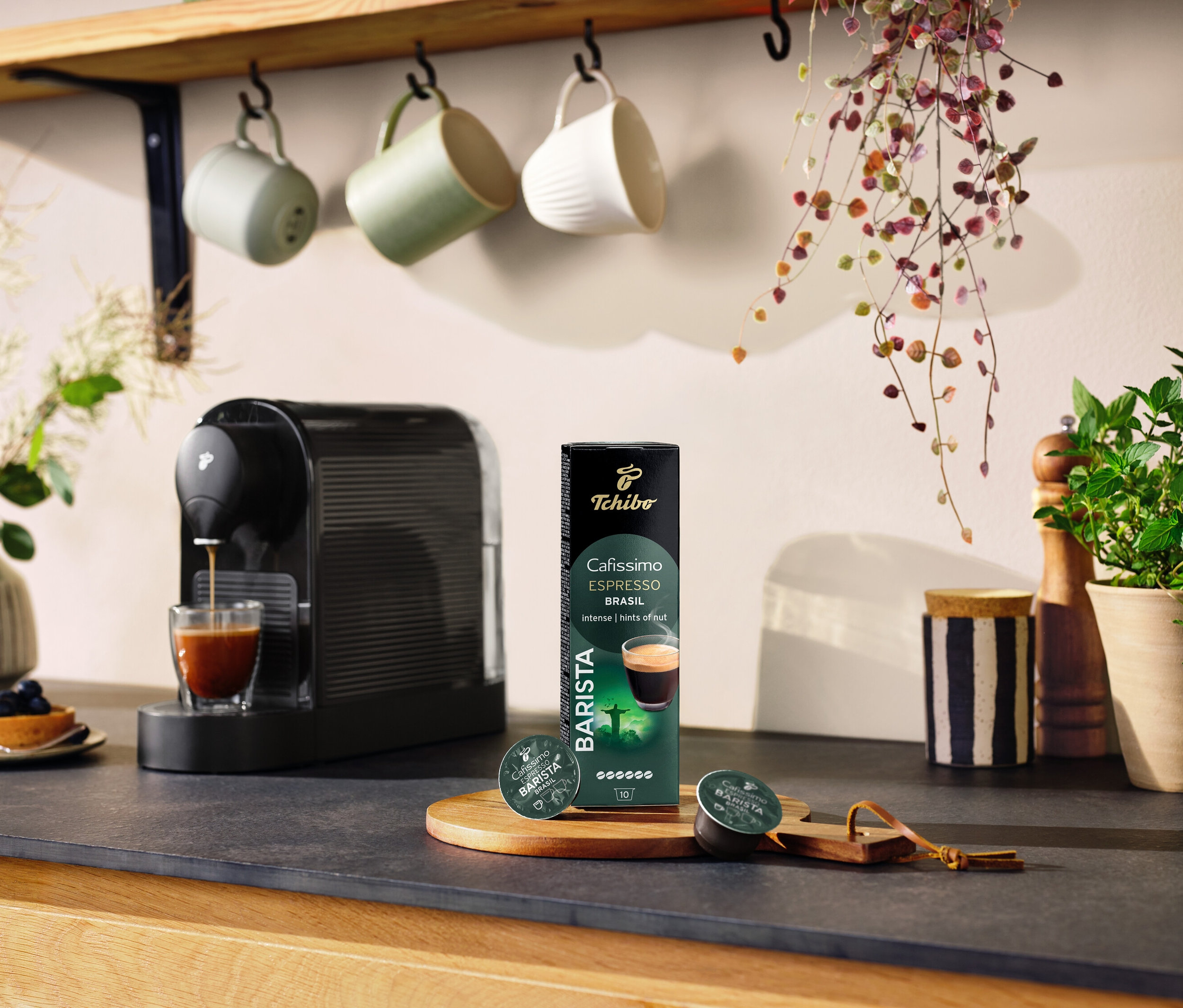 Schwarze Kaffeemaschine bereitet Kaffee in einem Glas neben einer Packung Cafissimo BARISTA Espresso Brasil - 10 Kapseln zu.