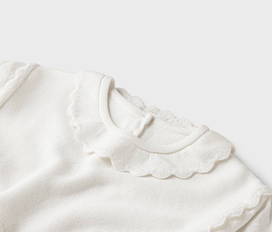 Nahaufnahme eines weißen Strickpullovers mit gewelltem Kragen.