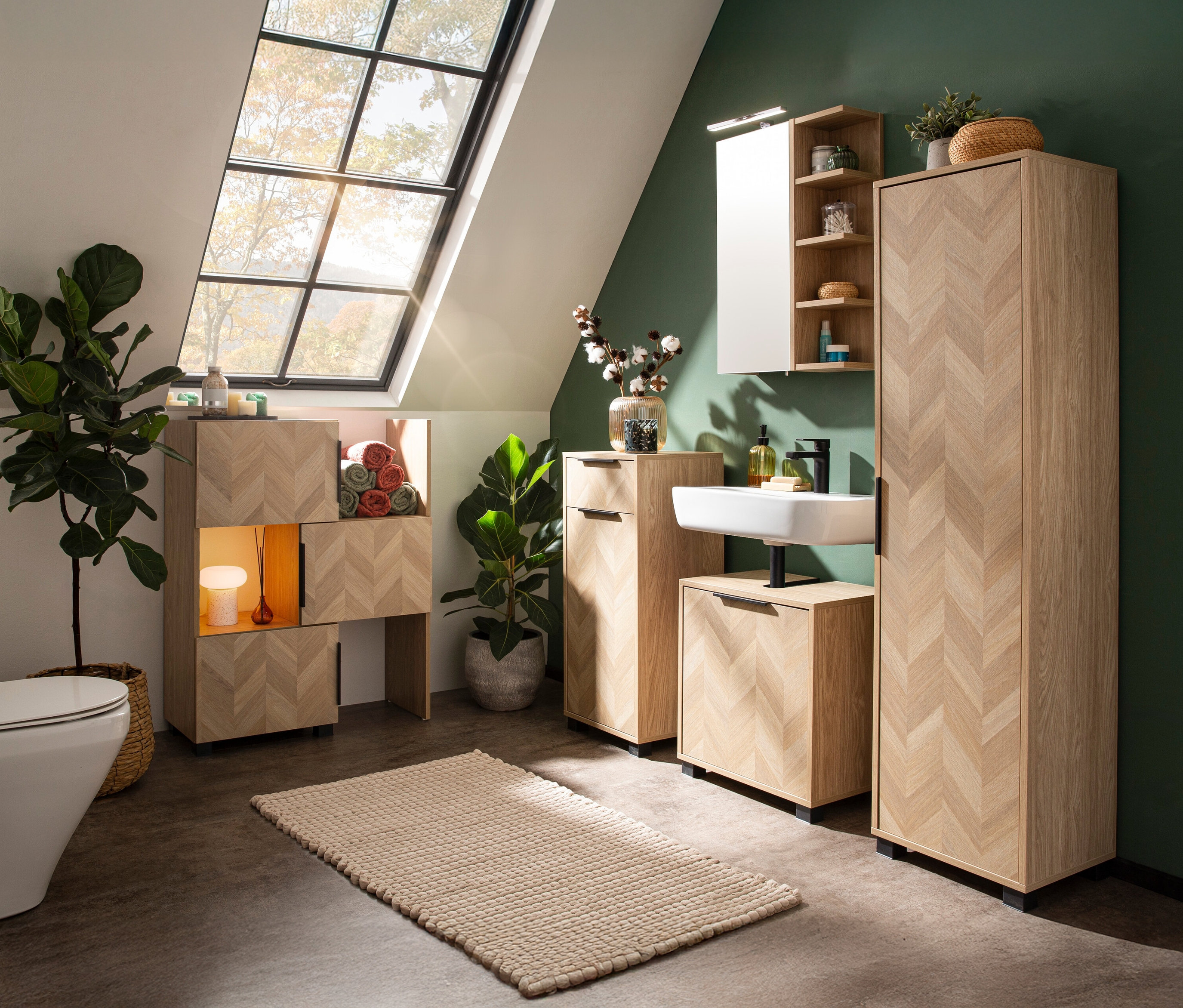 Ein Badezimmer mit hellen Holzmöbeln im Fischgrätenmuster, darunter ein Waschbeckenunterschrank, ein Hochschrank und ein Regal. Ein Fenster sorgt für Tageslicht.