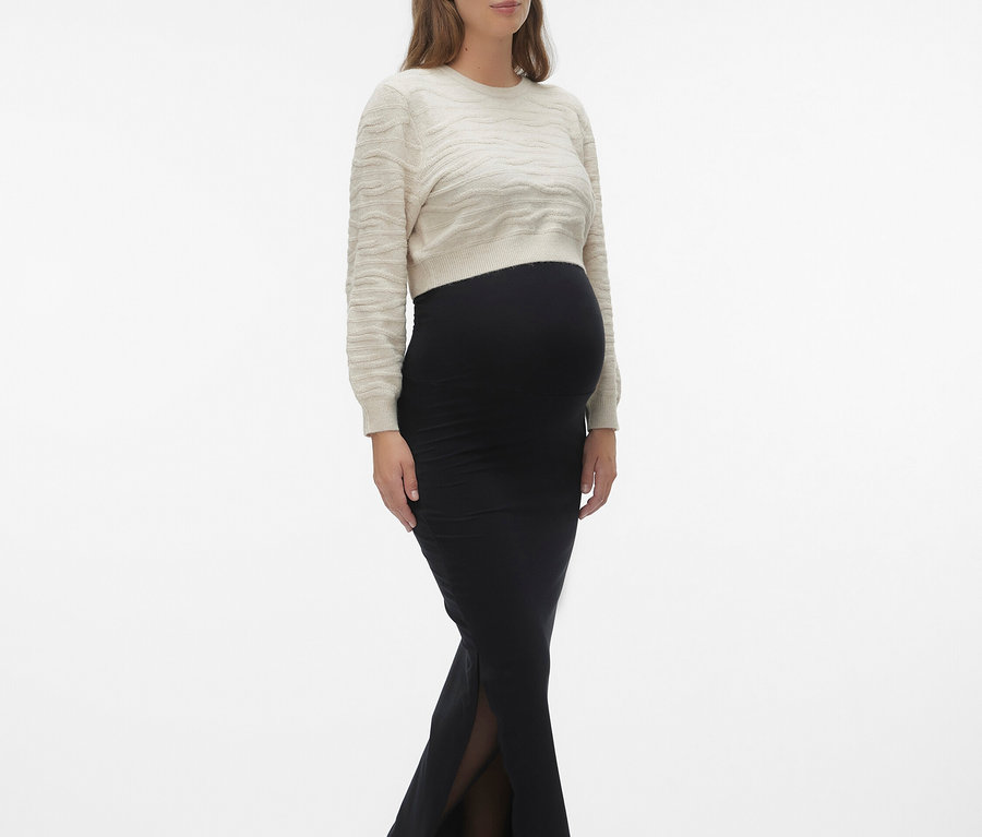 Schwangere Frau mit beigem Pullover und schwarzem Rock mit Schlitz, dazu schwarze Schuhe.