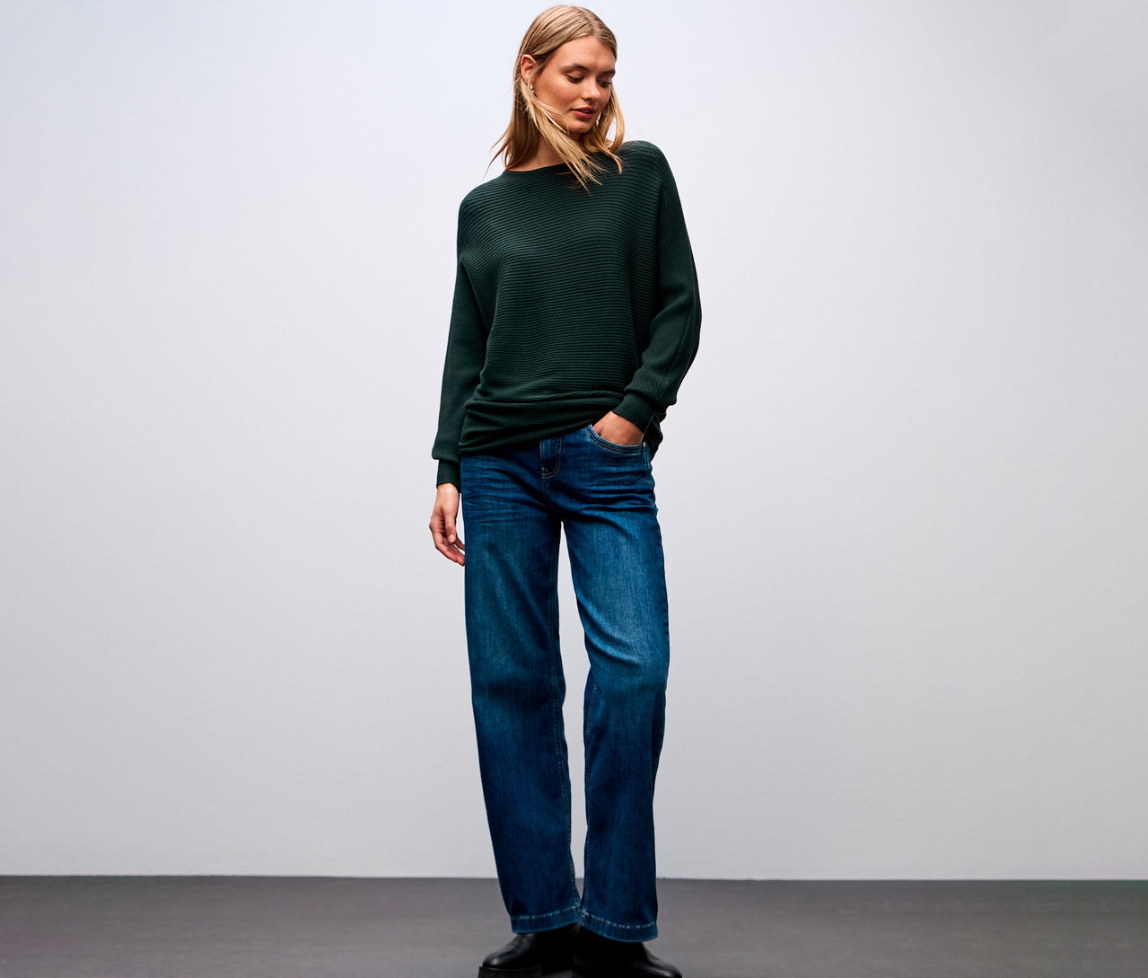Eine Frau trägt einen Street One Strukturpullover, Jeans und Schuhe.