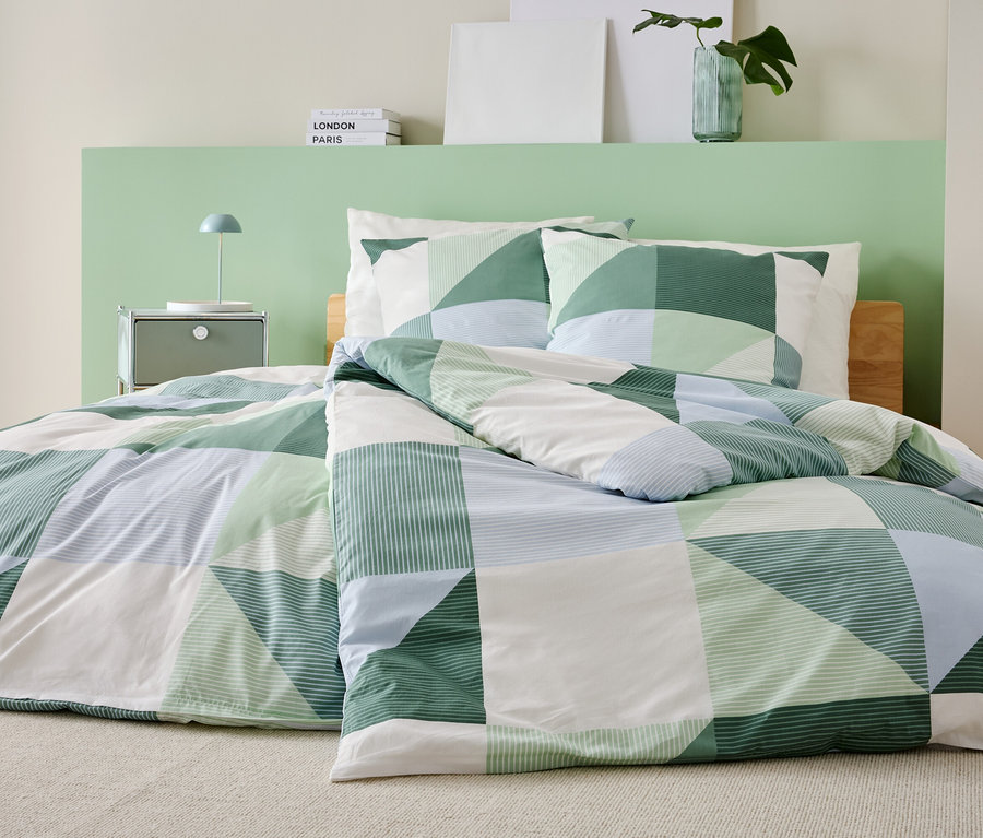 Ein Bett mit einer grün-weiß-blauen Patchwork-Bettdecke und passenden Kissenbezügen steht in einem Schlafzimmer.