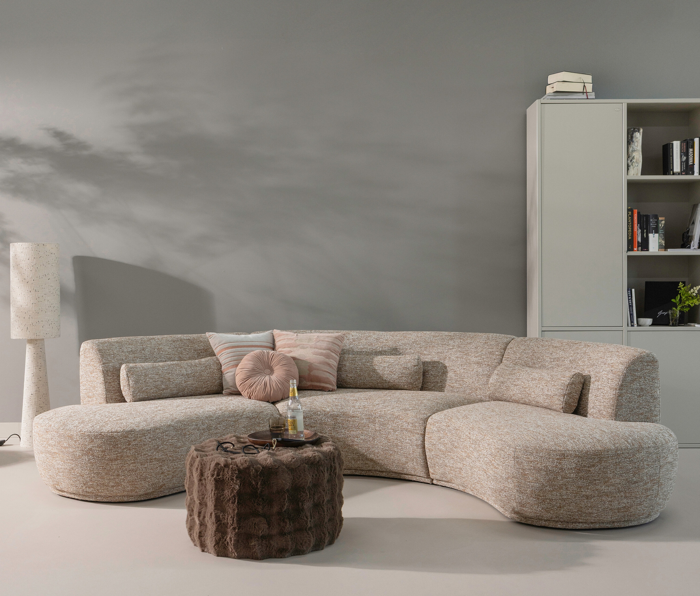 Ein brauner, niedriger Hocker »Olven« von WOOOD steht vor einem beigen Sofa mit Kissen. Auf dem Hocker stehen Getränke.