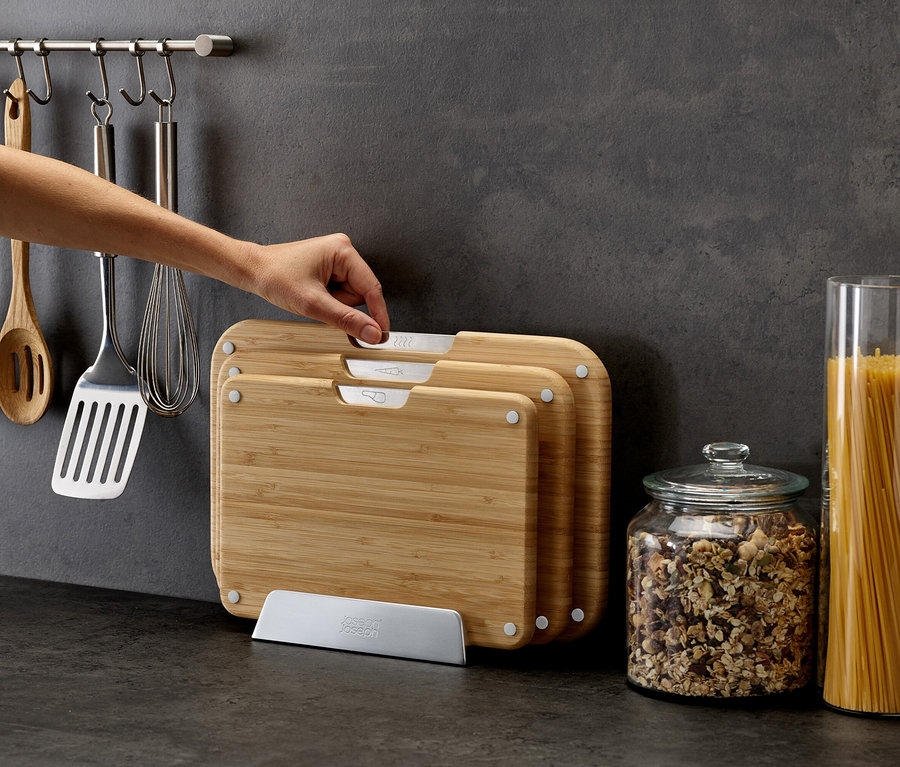 Hand nimmt ein Schneidebrett aus einem Set von Joseph Joseph. Auf der Arbeitsfläche stehen Vorratsgläser mit Müsli und Spaghetti.