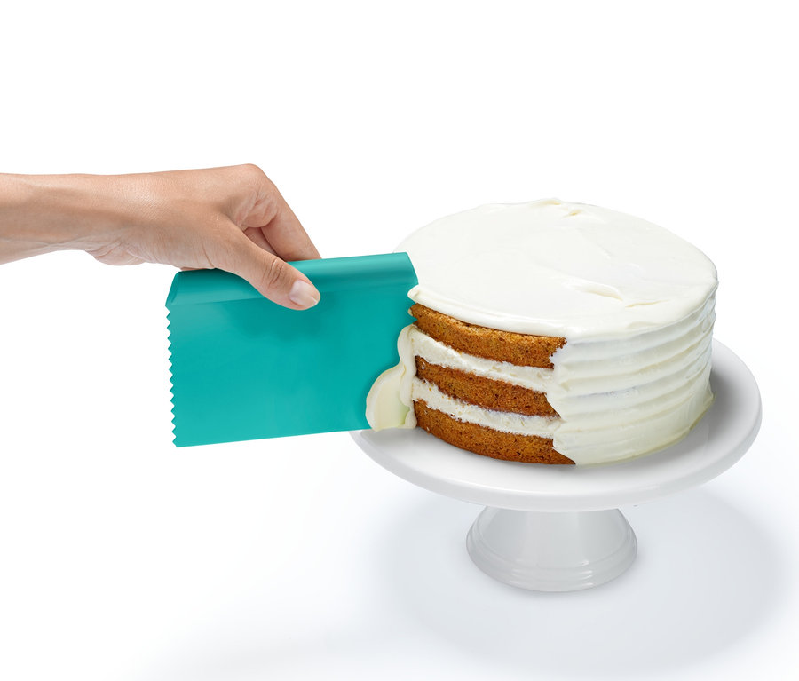 Eine Hand verteilt mit einem türkisfarbenen Spachtel aus dem Profi-Backhelfer-Set Zuckerguss auf einem dreischichtigen Kuchen.