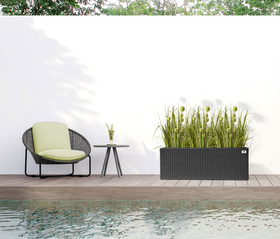 Ein Aussenbereich mit einem anthrazitfarbenen Polyrattan-Pflanzgefäß mit einer Breite von ca. 102 cm und Pflanzen.