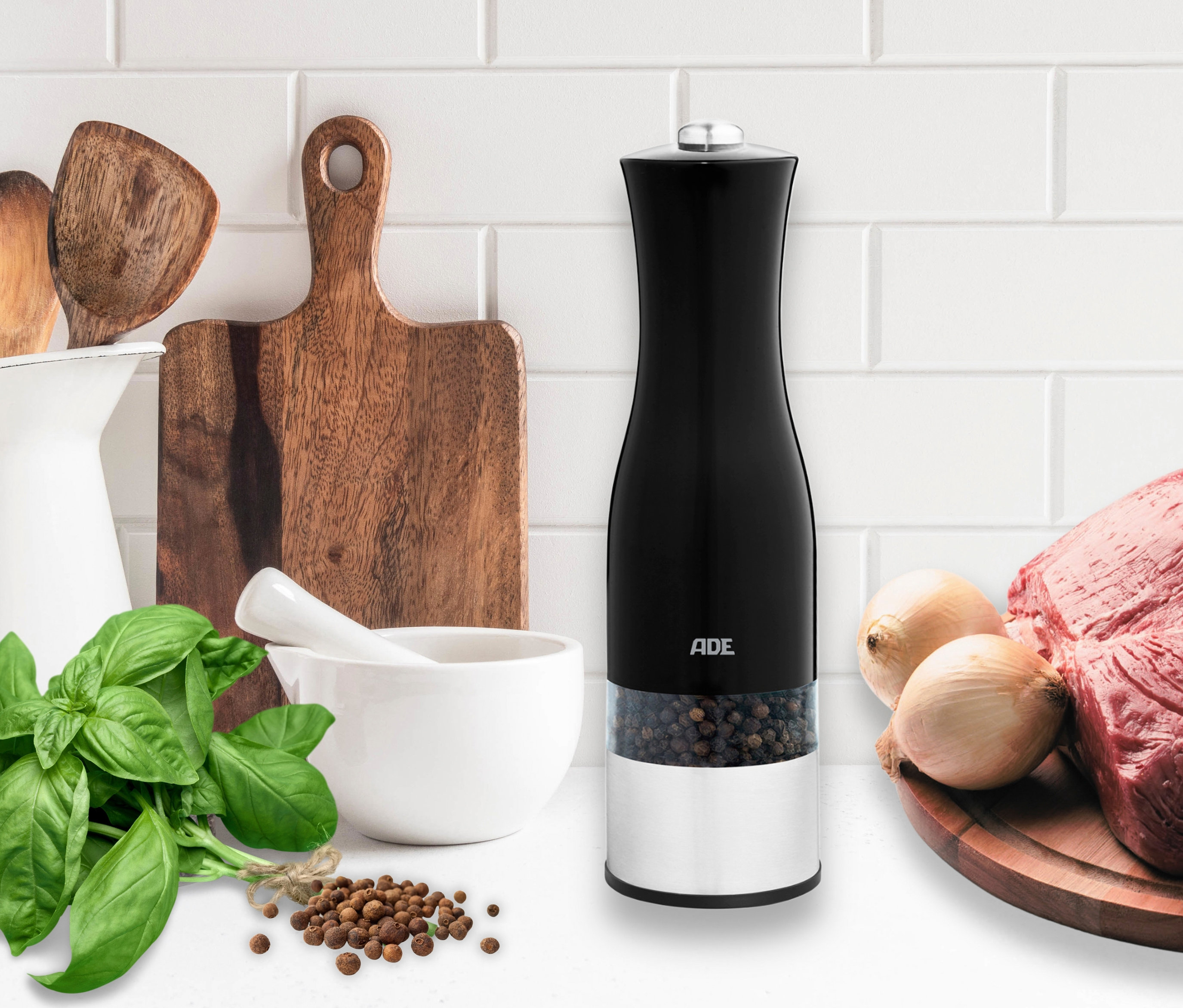 ADE Elektrische Salz-und-Pfeffermühle mit Beleuchtung, schwarz, steht auf einer Küchentheke neben Lebensmitteln.