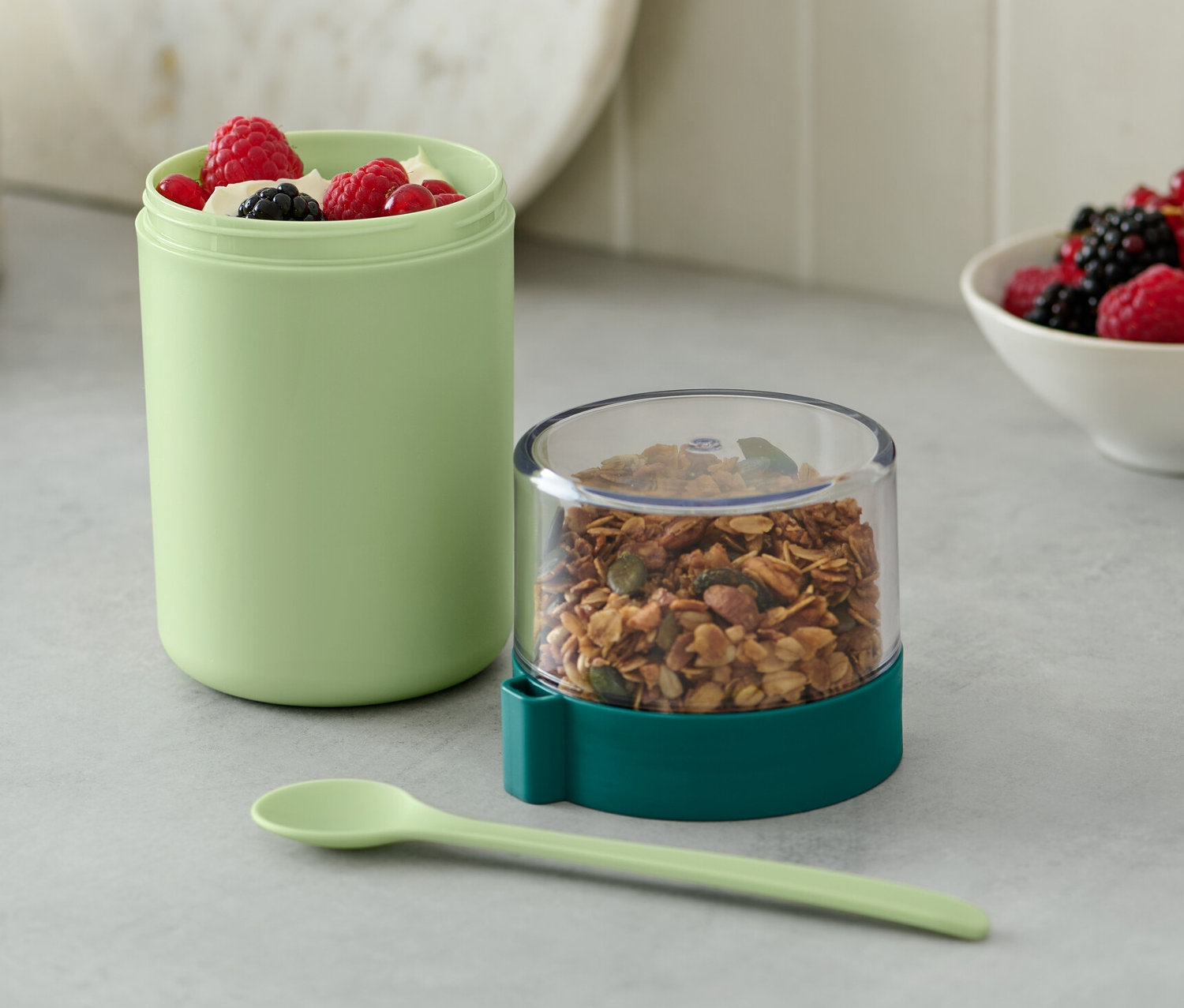 Ein grüner To-go-Joghurt-Becher mit Müsli und Beeren.