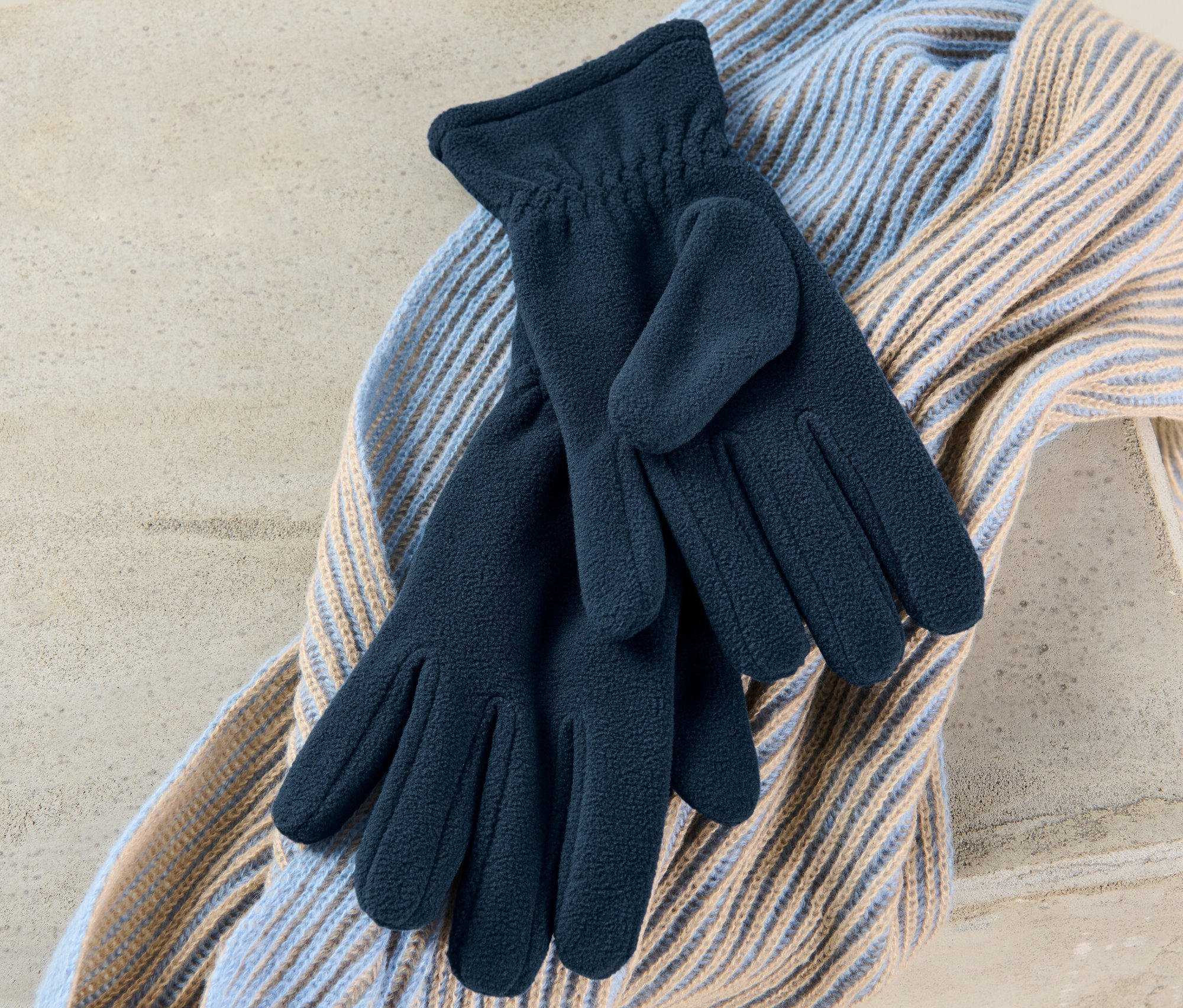 Ein Paar Fleece-Handschuhe liegen auf einem Schal.