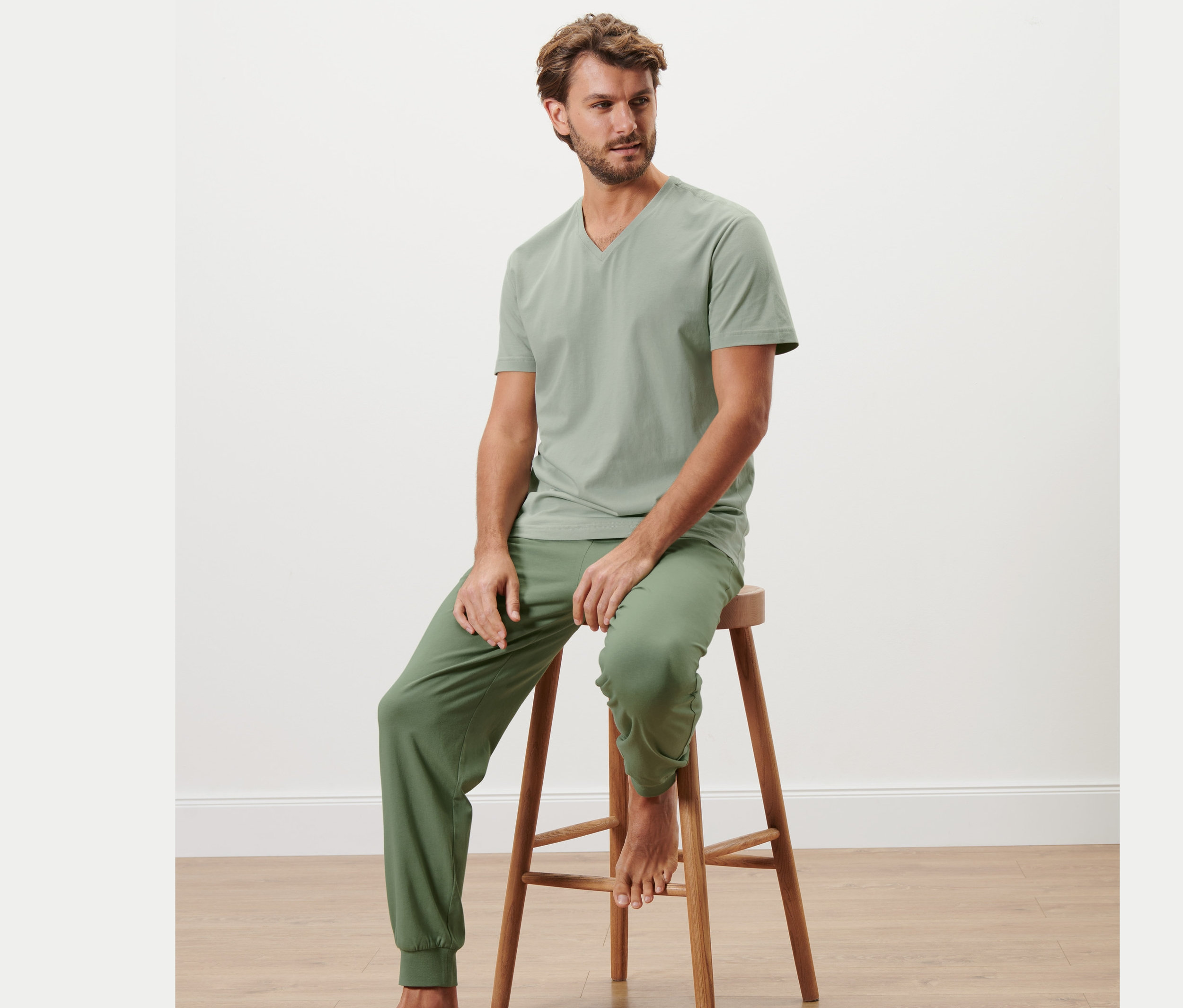 Mann sitzt auf einem Holzhocker und trägt einen Pyjama.