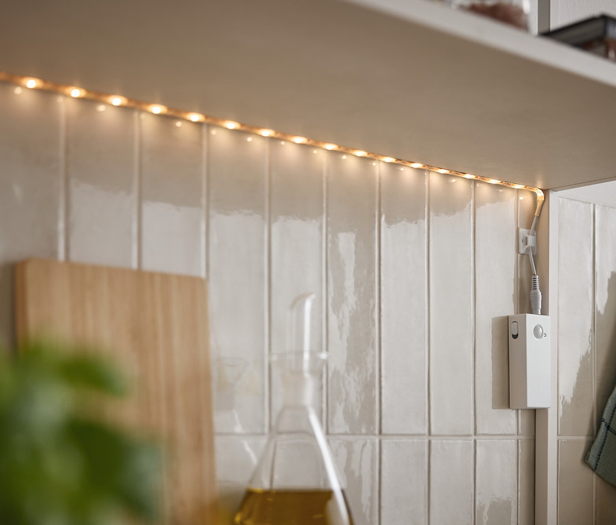 LED-Streifen leuchtet unter einem Schrank an weißen Fliesen.
