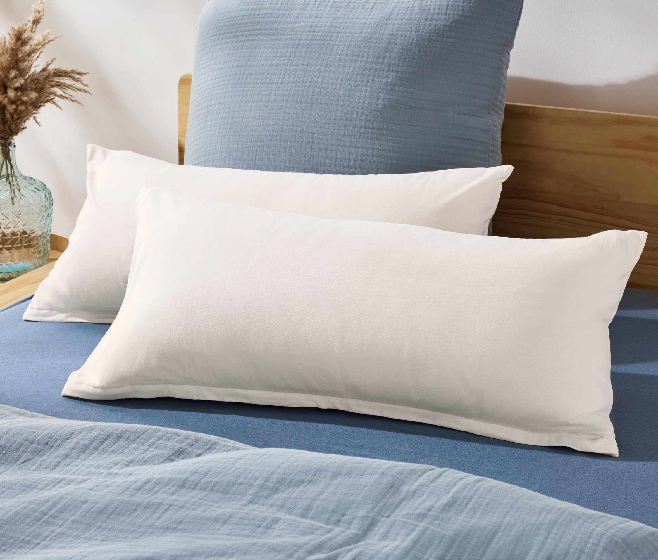 Zwei Jersey-Kopfkissenbezüge liegen auf einem Bett mit blauem Bettlaken und Bettdecke.