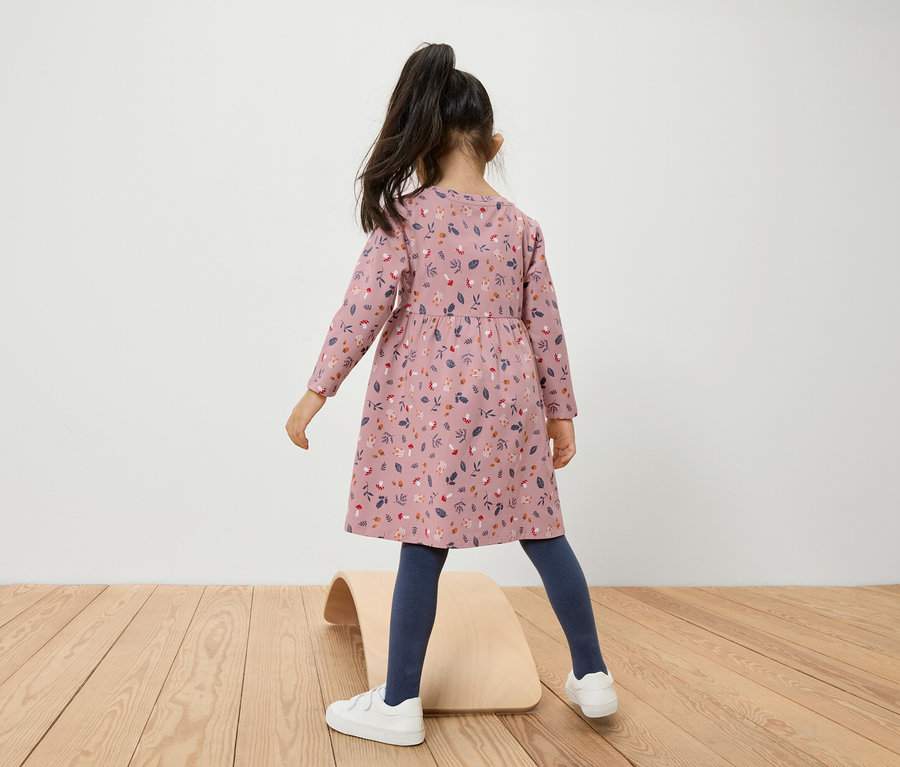 Mädchen im geblümten Kleid steht auf einem hölzernen Balance Board.