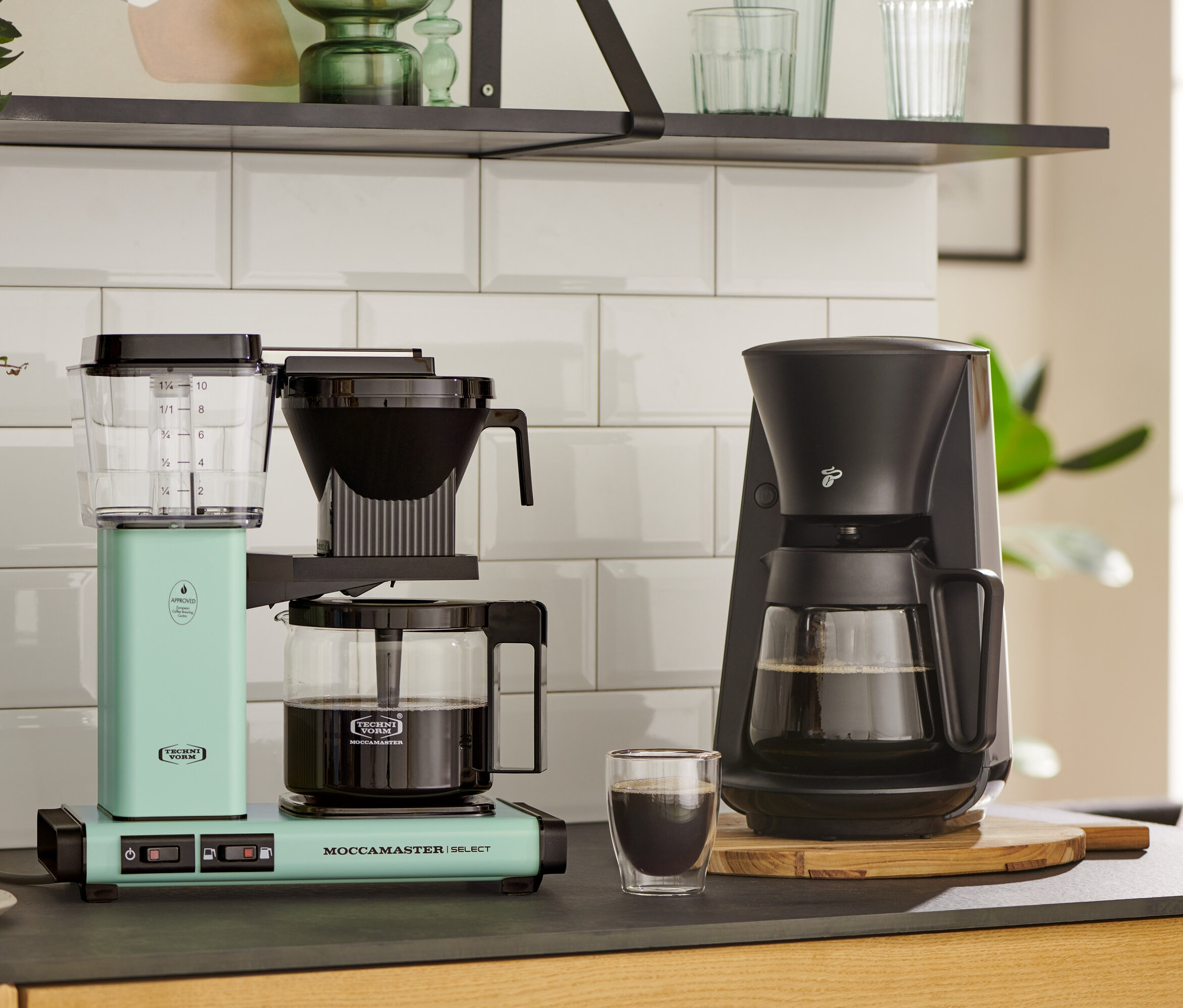 Zwei Kaffeemaschinen auf einer Küchentheke: eine pastellgrüne Moccamaster KBG Select Filterkaffeemaschine und eine schwarze.