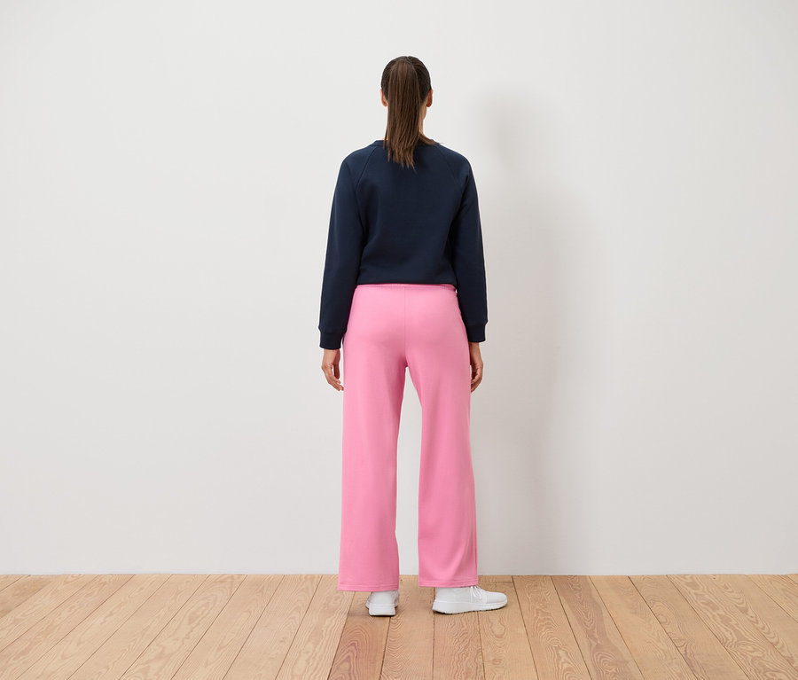 Eine Frau steht mit dem Rücken zur Kamera und trägt ein dunkelblaues Sweatshirt und eine rosafarbene Hose.