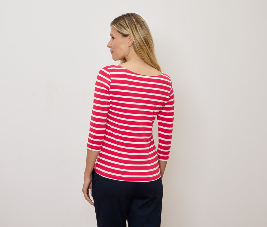 Blonde Frau schaut nach links und trägt ein rot-weiß gestreiftes Dreiviertelarm-Shirt.