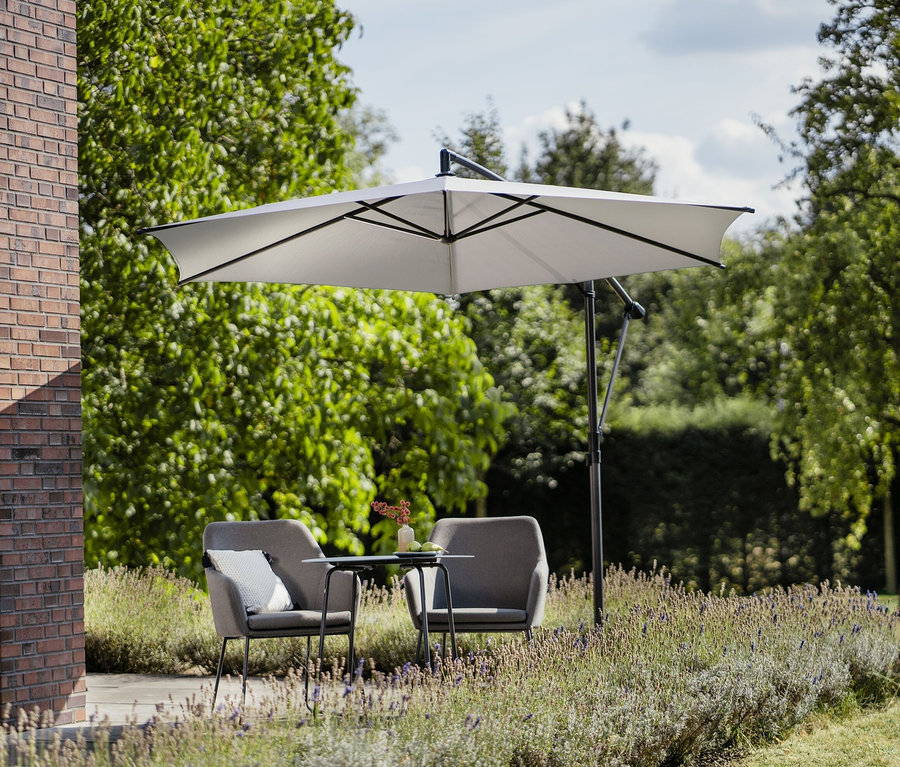 Zwei graue Sessel und ein Tisch stehen draußen unter einem hellgrauen Leco Ampelschirm Ø 300 cm, inkl. Schirmständer und Abdeckhaube.