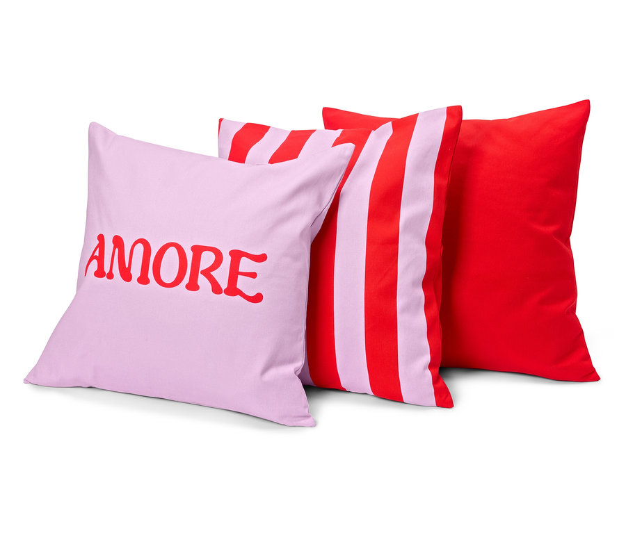 Drei Kissen: ein lilafarbenes mit dem roten Wort 'AMORE', ein gestreiftes, rot-lila und einfarbig rot.