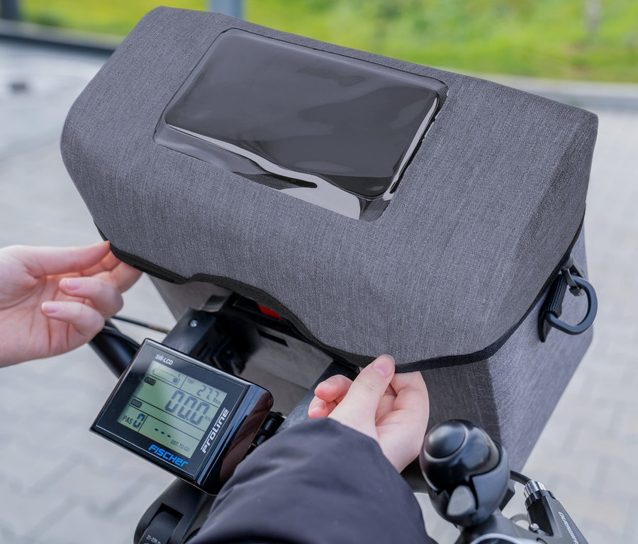 Hände befestigen eine graue FISCHER Lenkertasche PLUS Cita an einem Fahrradlenker.