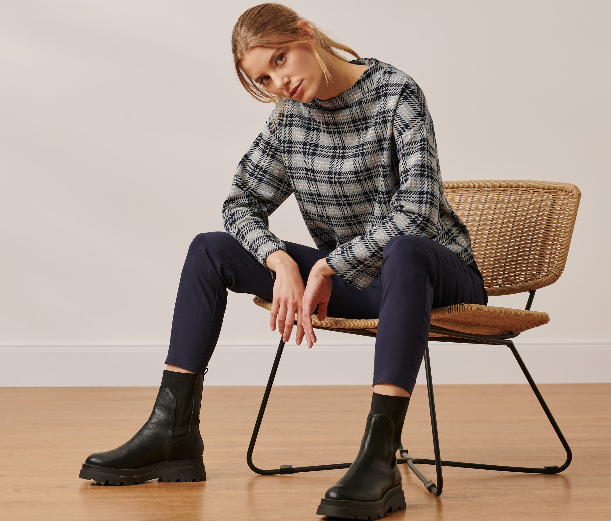 Frau sitzt auf einem Korbstuhl und trägt ein kariertes Sweatshirt.