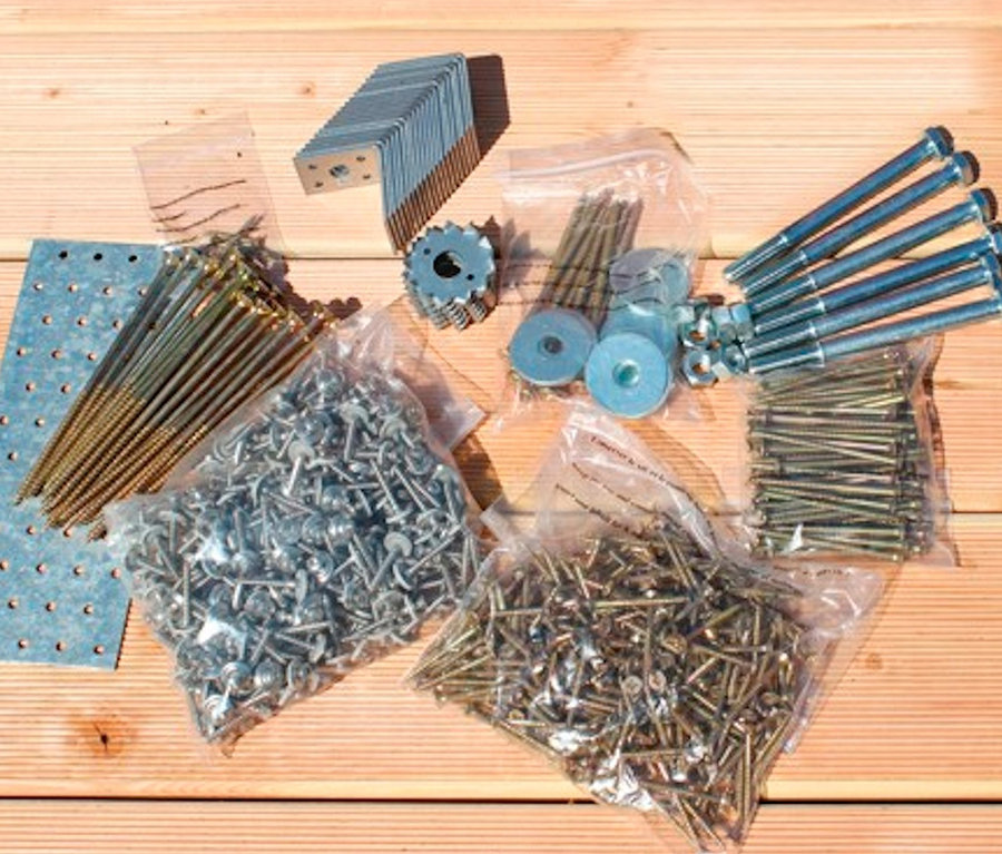 Verschiedene Befestigungselemente, darunter Schrauben, Nägel und Halterungen, sind auf einer Holzoberfläche angeordnet. Karibu Carport mit Abstellraum, Seiten und Rückwand, 19 mm, (Elco 2)