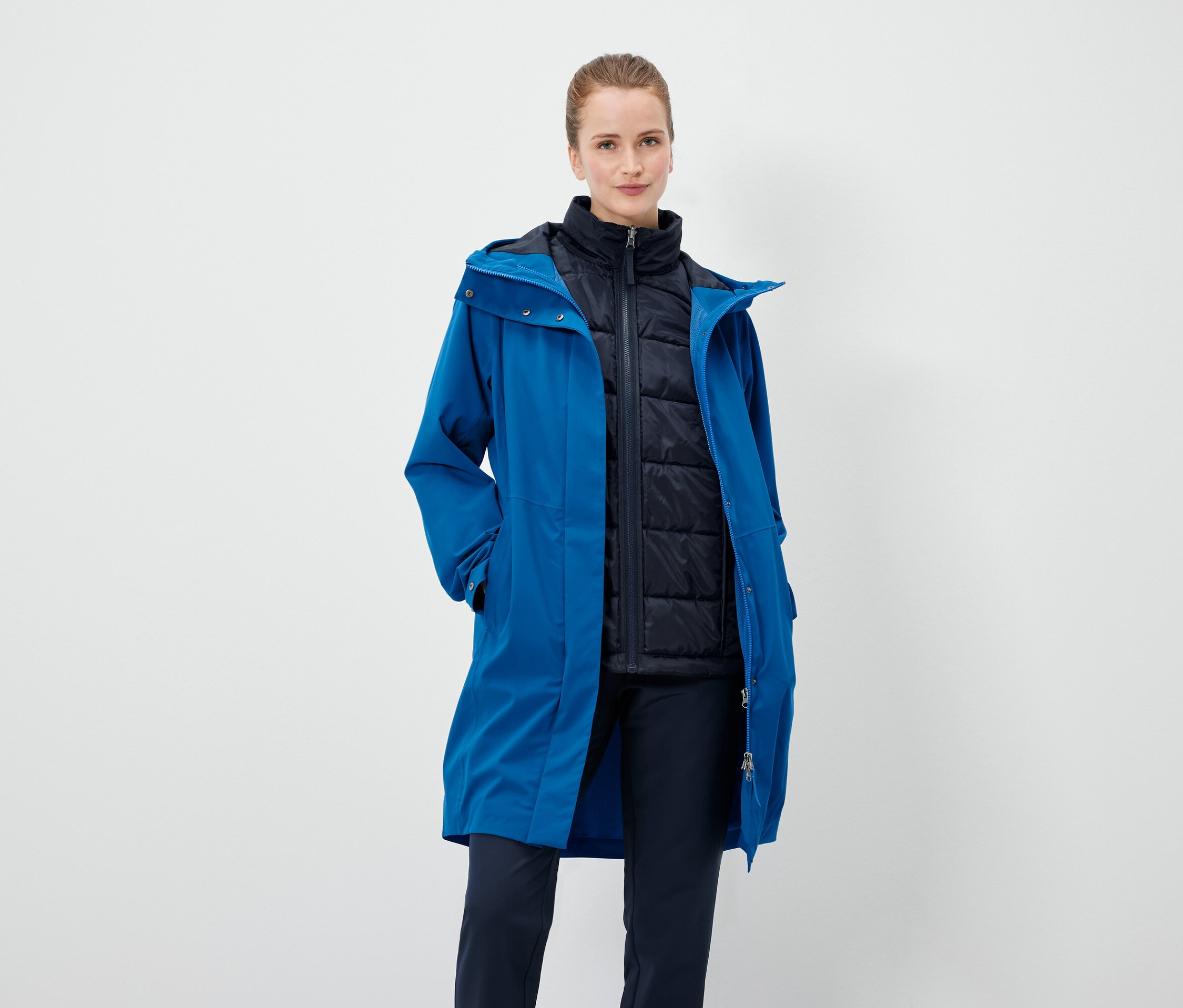 Eine Frau trägt einen blauen Mantel und eine schwarze Weste.