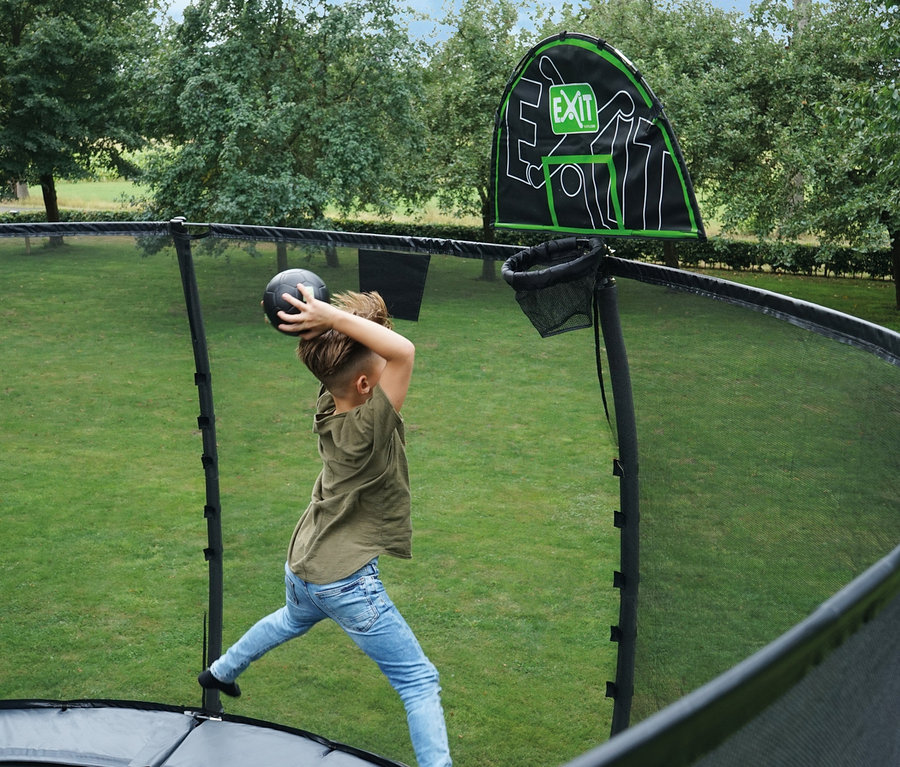 Ein Junge wirft einen Ball auf einen grün-schwarzen EXIT Trampolin-Korb auf einem Trampolin.