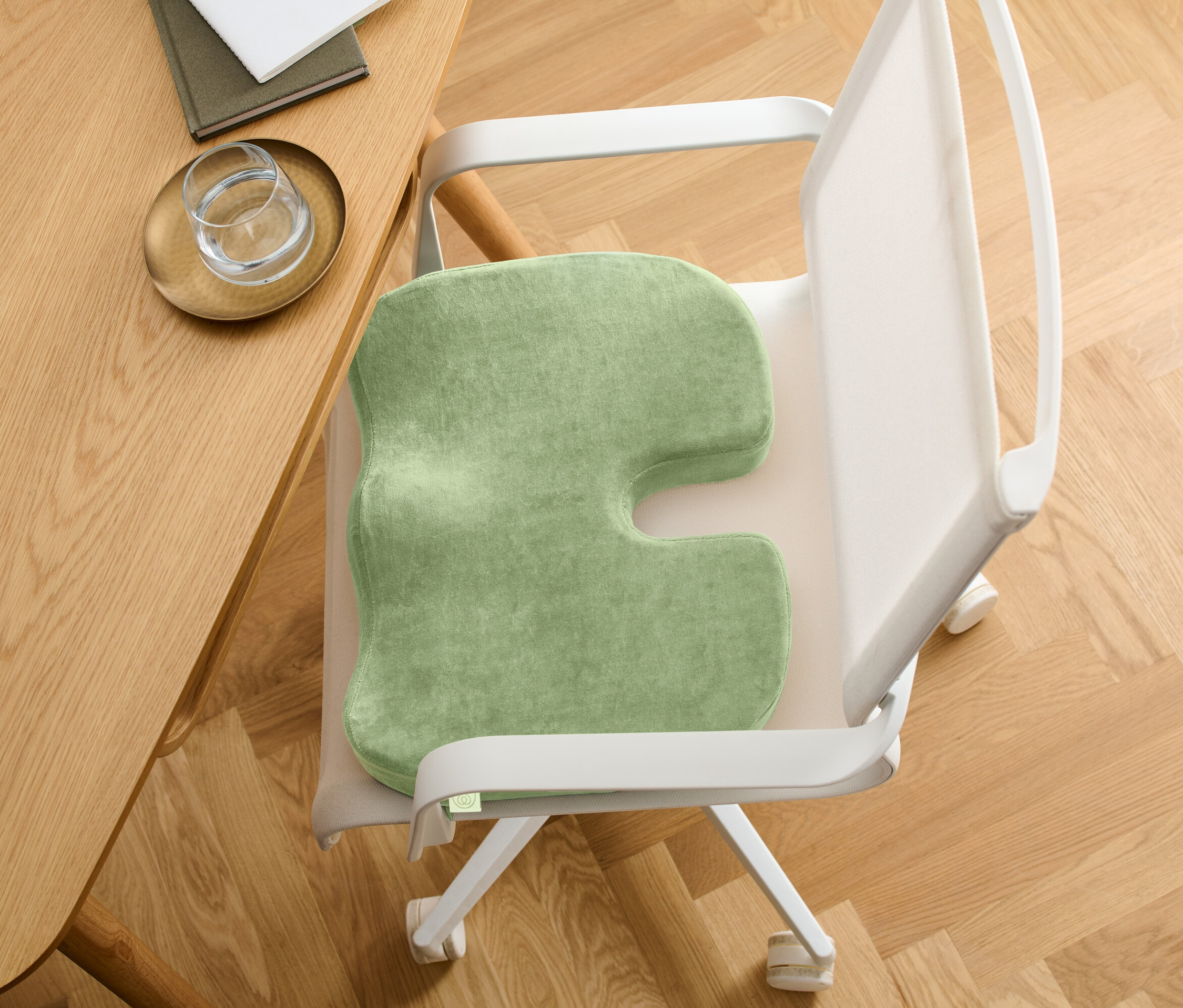 Grünes Sitzkissen mit U-förmigem Ausschnitt auf einem Stuhl. Der Stuhl steht an einem Holztisch.