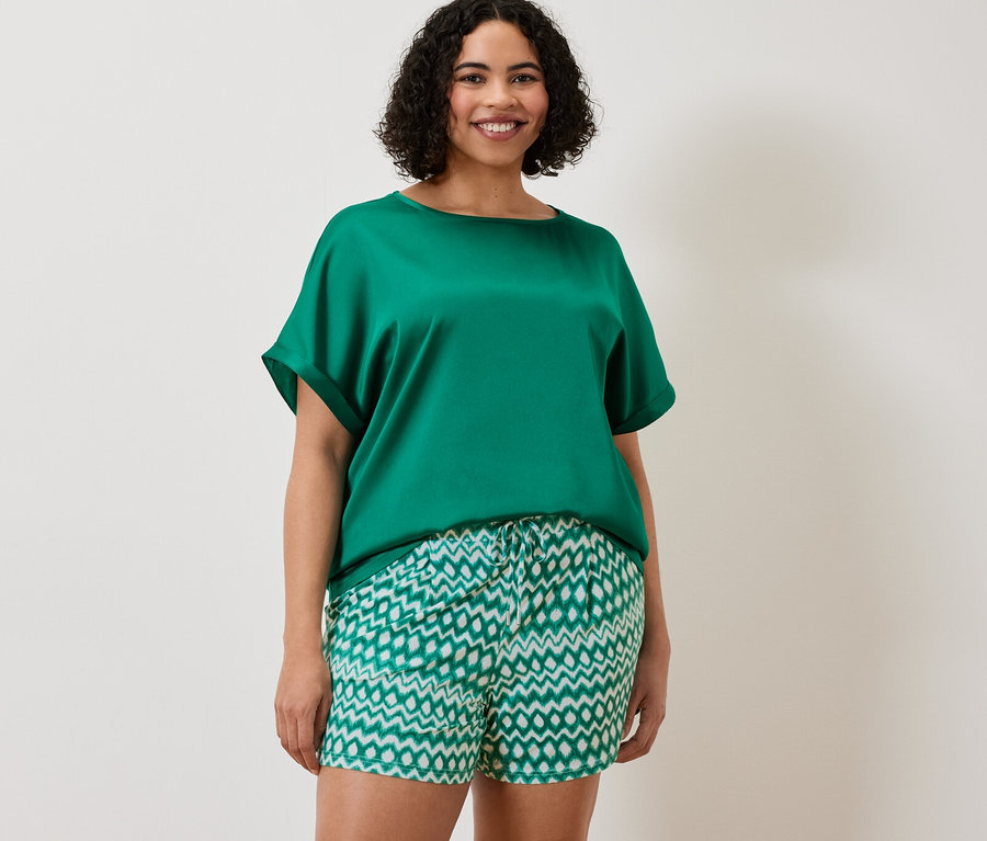 Frau trägt ein aquafarbenes Blusenshirt im Materialmix und 2 Jerseyshorts.