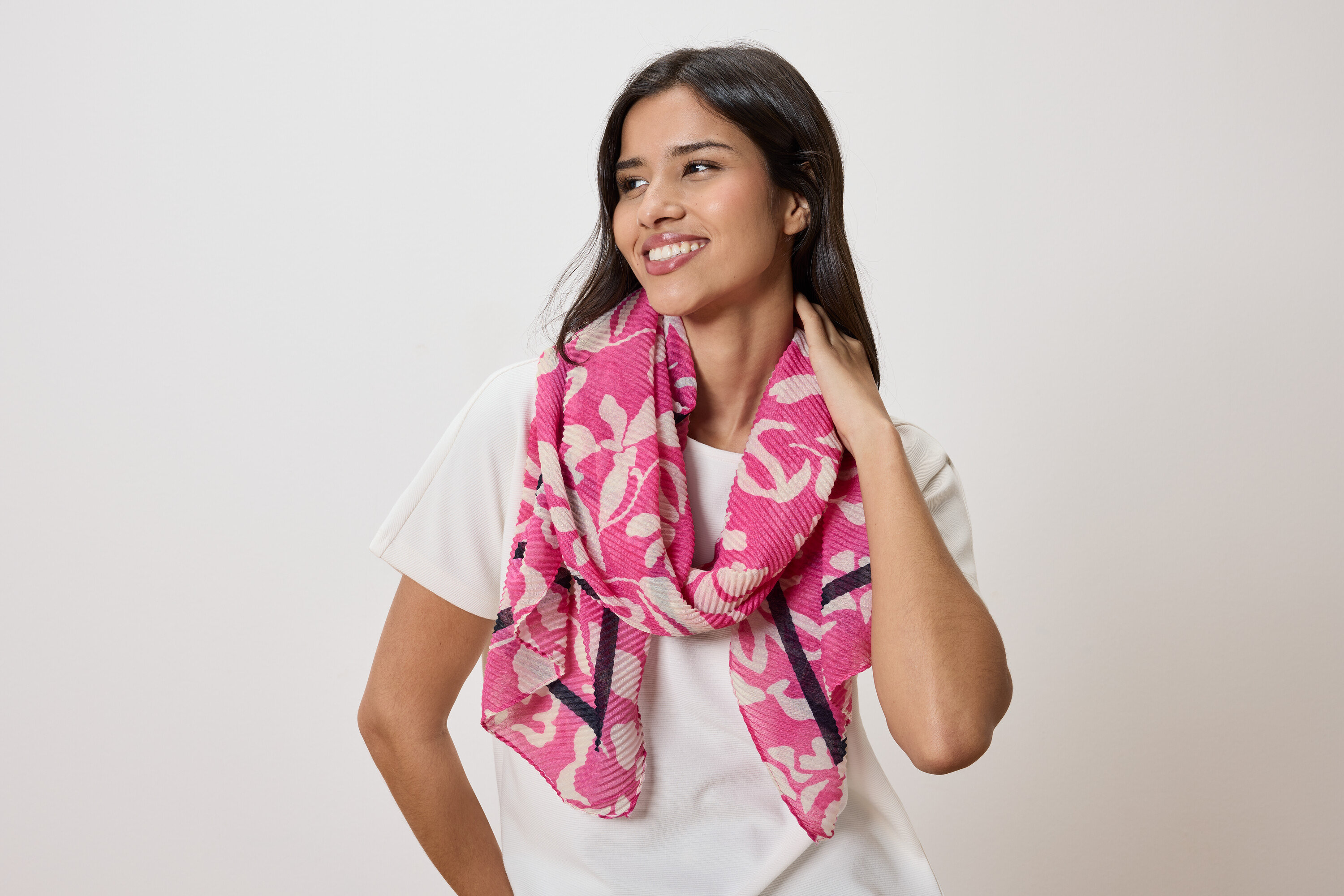 Frau mit einem pinkfarbenen Schal mit Blumenmuster und einem weißen T-Shirt.