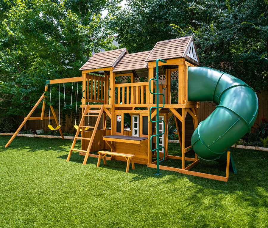 Der Spielturm »Bolzo« steht auf einem grünen Rasen vor Bäumen.