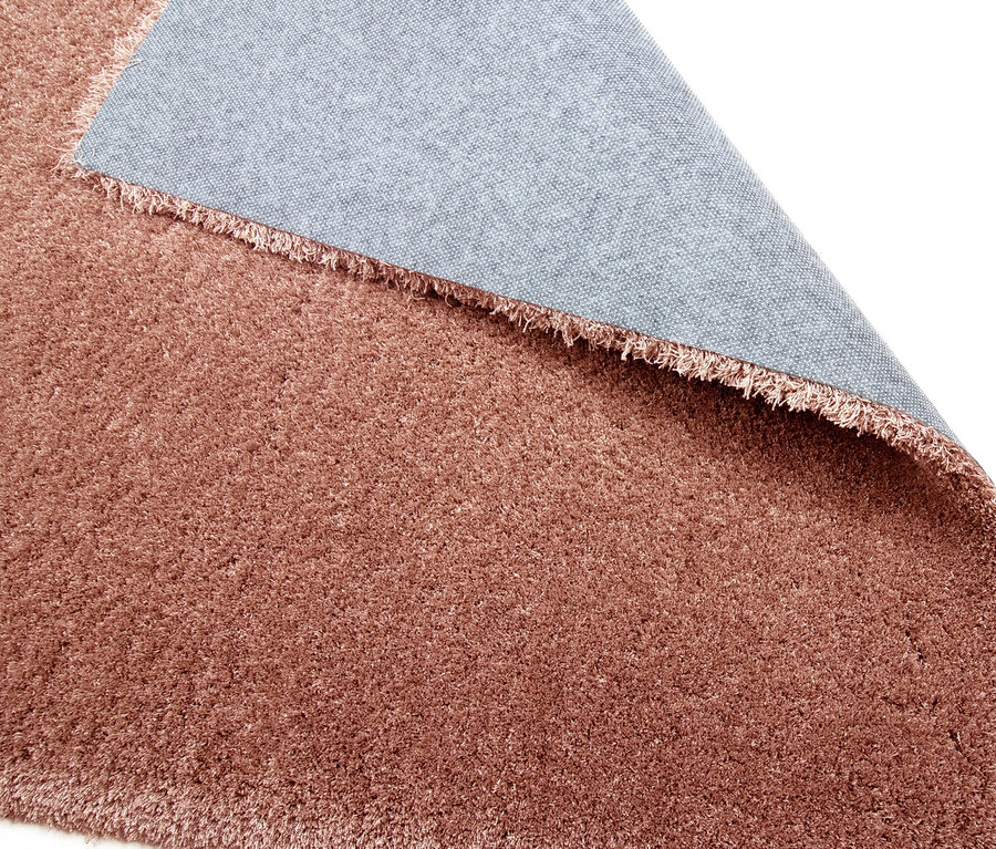 Nahaufnahme eines rostfarbenen Teppichs »Pleasure« mit hochgeklappter Ecke, die die graue Unterseite zeigt.