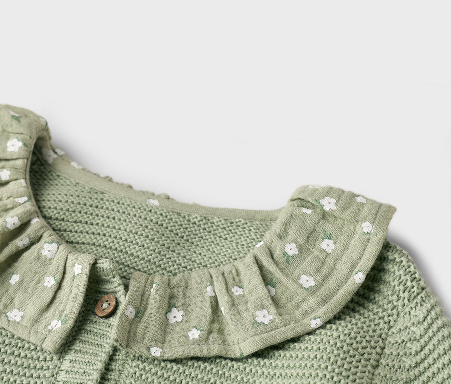 Nahaufnahme einer hellgrünen Strickjacke mit weißem Blumenmuster und Rüschenkragen.