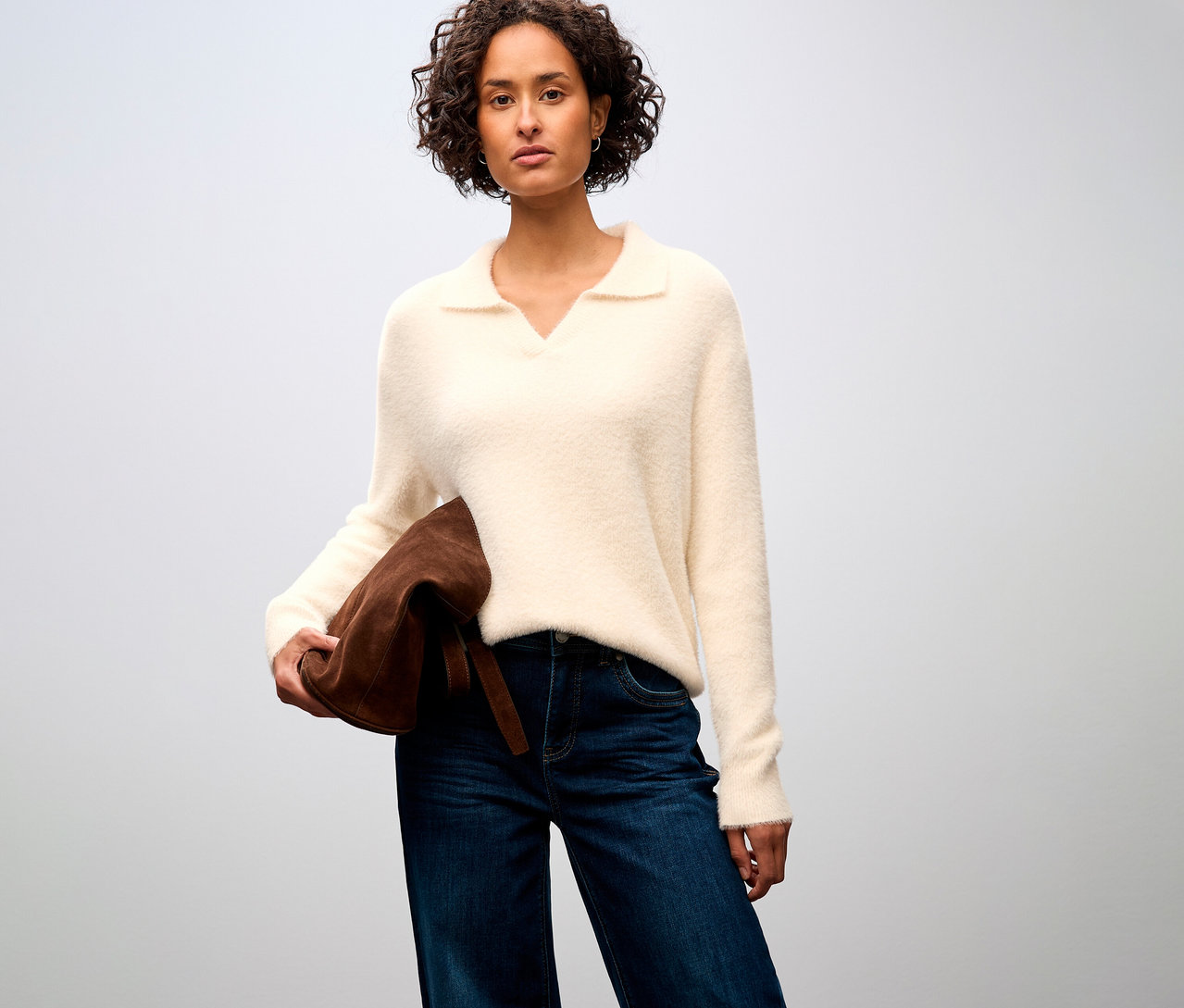 Frau trägt einen Street One Strickpullover mit Polokragen, Jeans und hält eine braune Tasche.