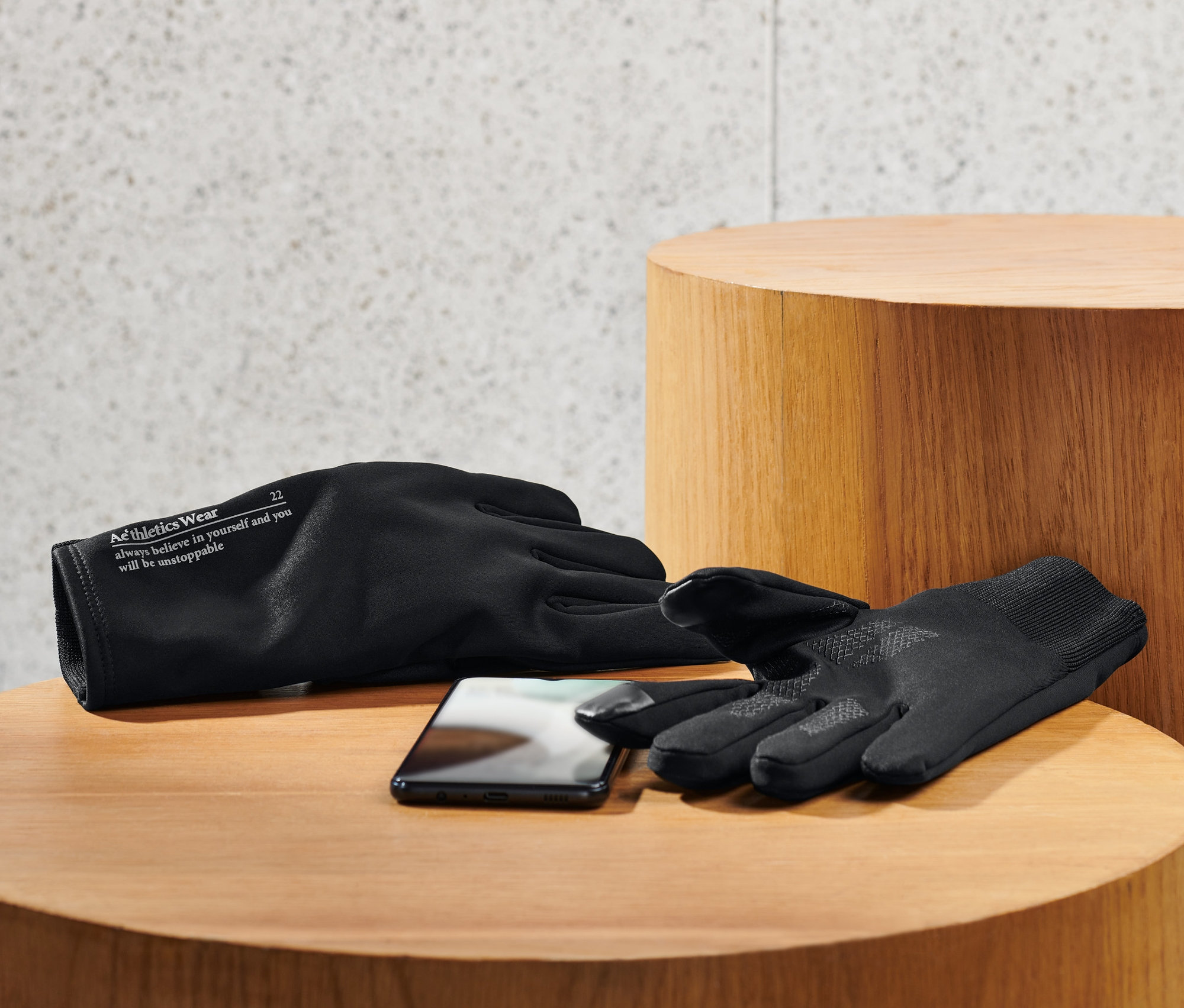 Zwei schwarze Windprotection-Handschuhe und ein Mobiltelefon liegen auf einem Holztisch.