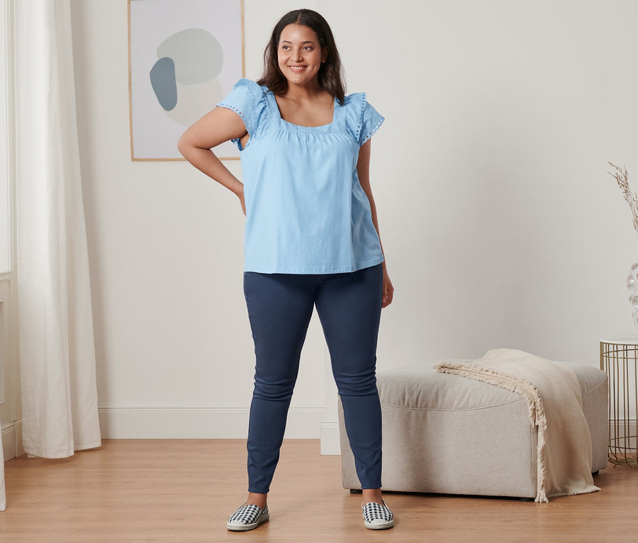 Frau posiert in hellblauem Shirt mit Stickerei, Jeggings und Espadrilles.