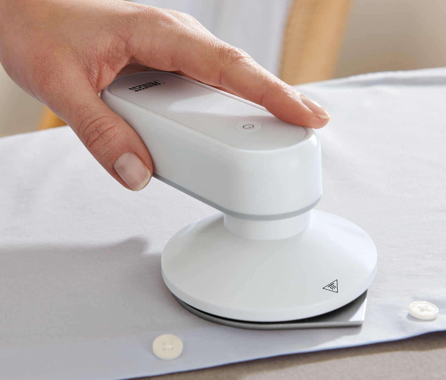 Eine Hand bügelt ein weisses Hemd mit einem Princess-Reisebügeleisen mit Powerbank.