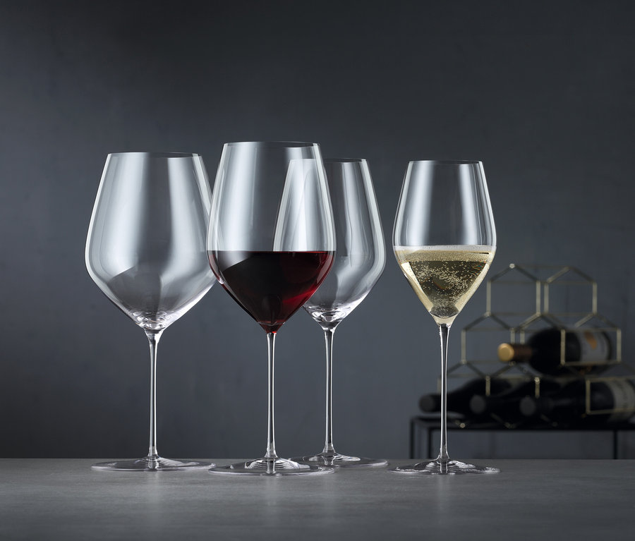 Vier Spiegelau Hi-Lite Gläser: leer, Rotwein, leer und Champagner. Im Hintergrund ein Weinregal.