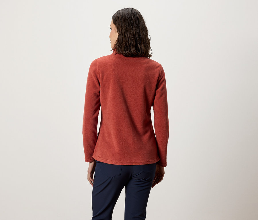 Eine Frau mit dem Rücken zur Kamera trägt ein orangefarbenes Fleece-Oberteil und marineblaue Hosen.