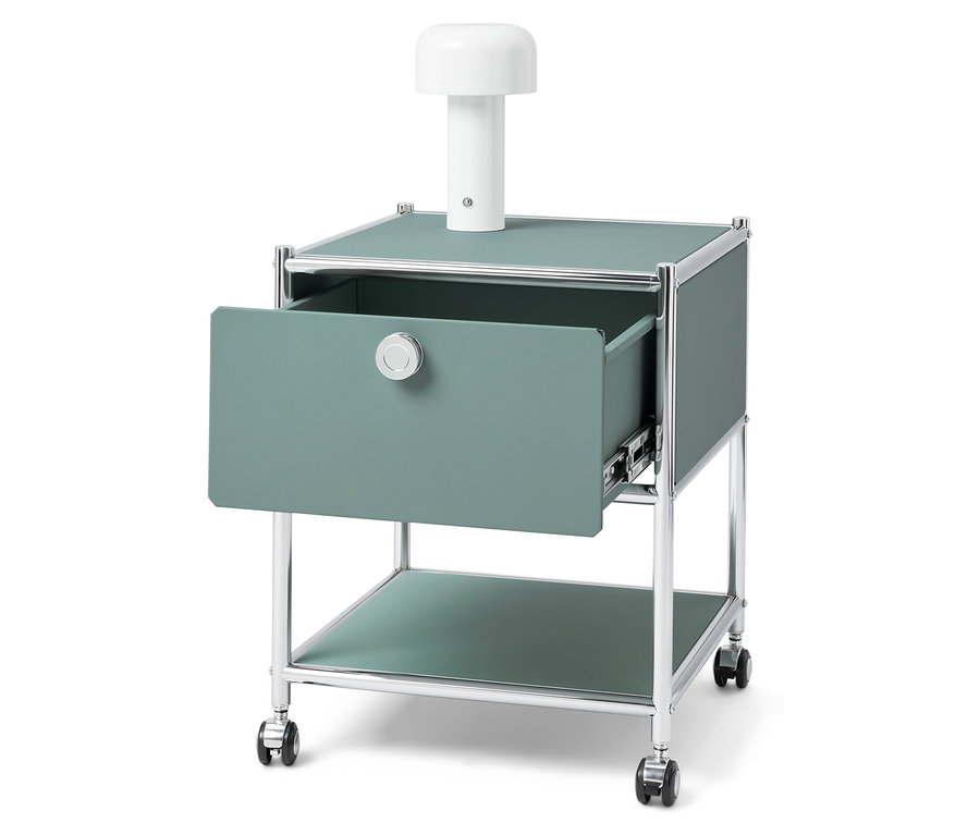 Grüner Nachttisch mit offener Schublade und weißer Lampe darauf.