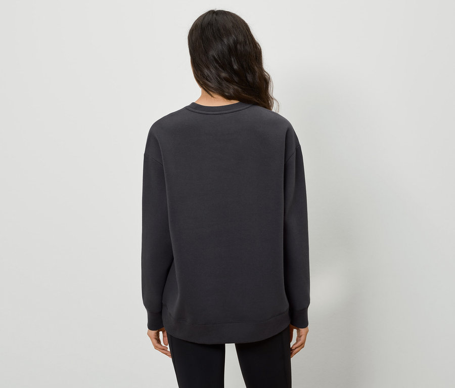 Rückansicht einer Frau mit dunklen Haaren, die einen schwarzen Pullover und schwarze Hosen trägt.