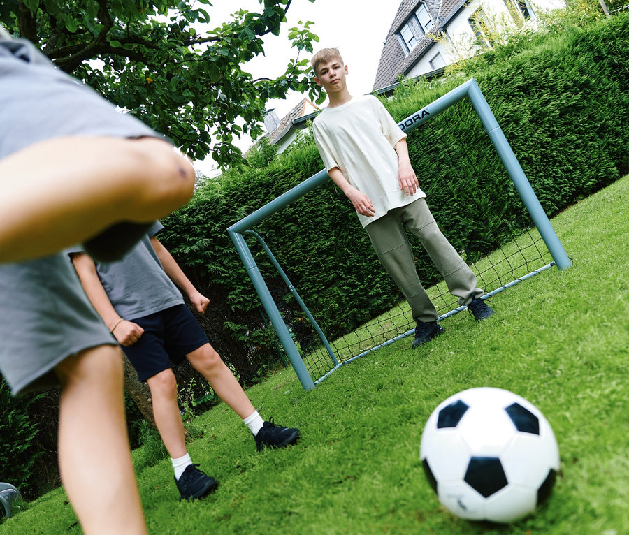 Jungen spielen Fußball mit einem HUDORA Fußballtor »Expert 240« auf einer Wiese.