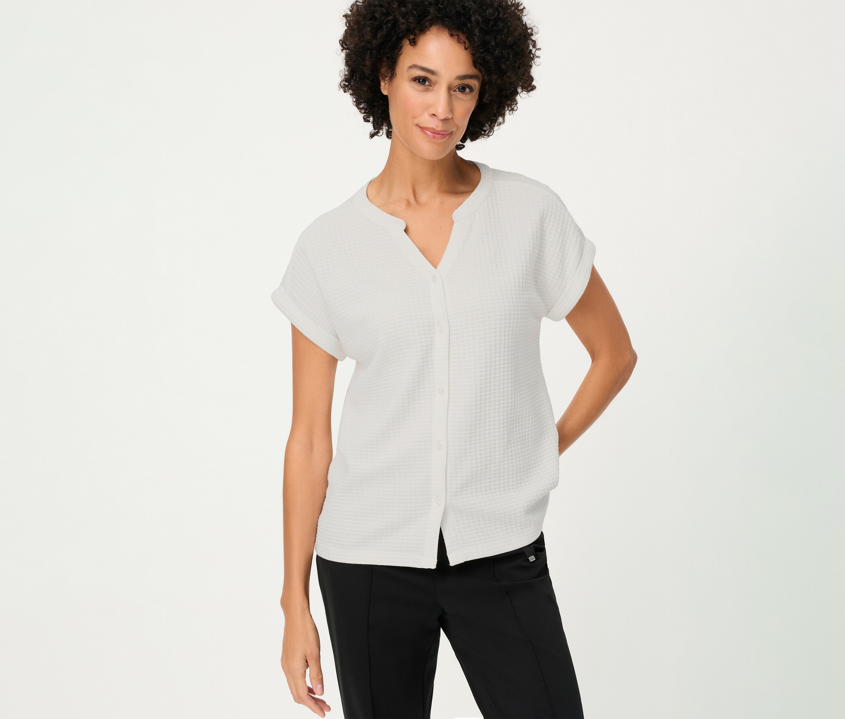 Frau mit lockigem Haar trägt ein strukturiertes Olsen Shirt mit Knöpfen in Weiß und schwarze Hose.