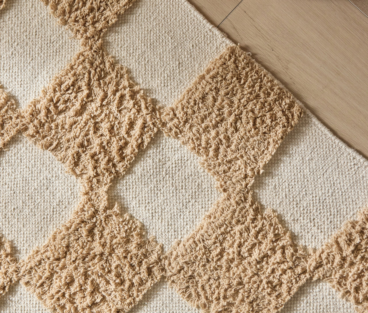 Detailansicht eines Teppichs mit beigen Rauten auf einem cremefarbenen Untergrund.