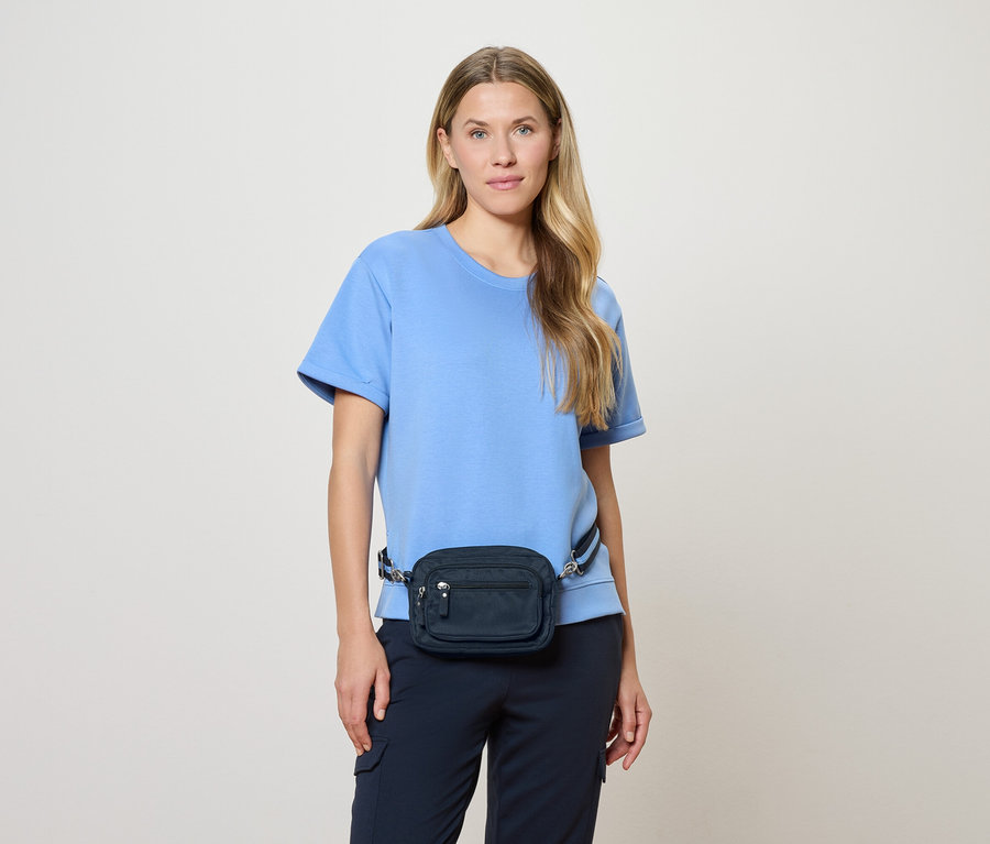 Frau mit hellblauem Oberteil und marineblauer Bauchtasche vor hellem Hintergrund.