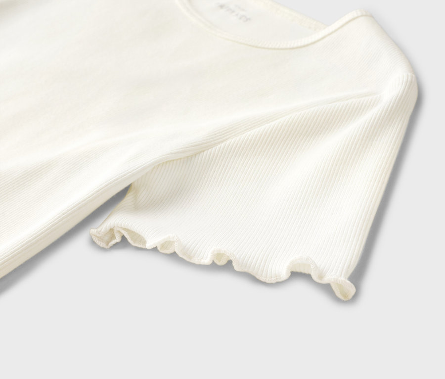 Detailansicht eines gerippten, cremefarbenen Oberteils mit kurzen Ärmeln und Rüschensaum.