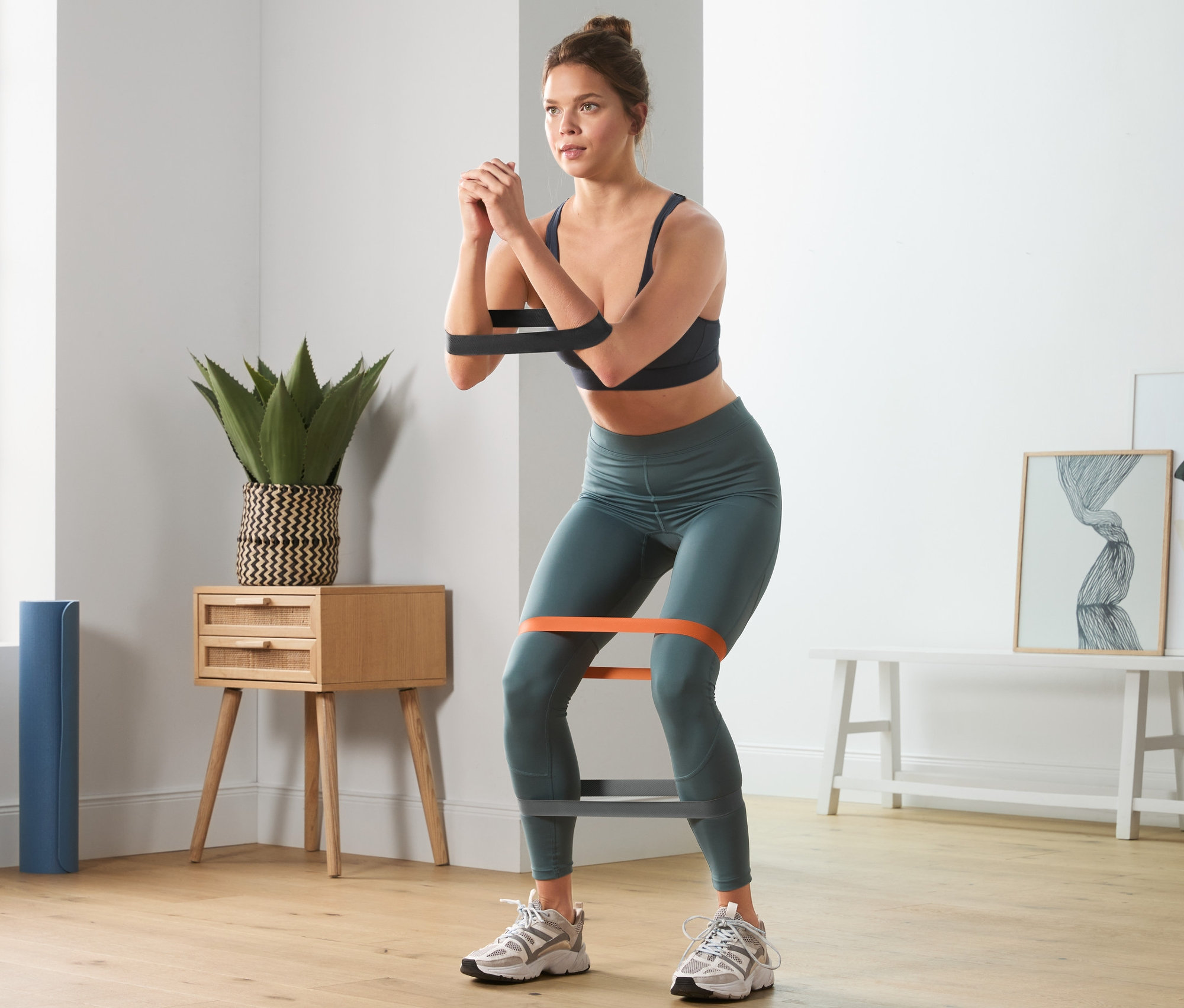 Frau macht Kniebeugen mit 3 Trainingsbändern.